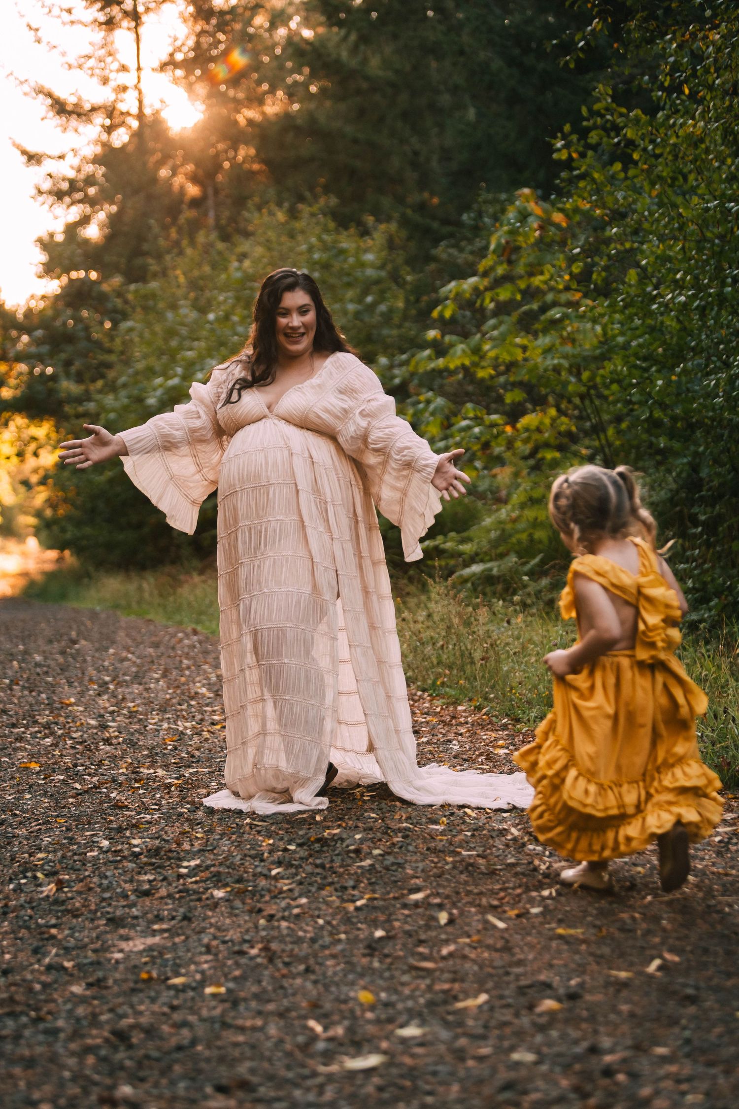 Two people in flowing dresses dance together at sunset in a wooded area with fallen autumn leaves on the ground.