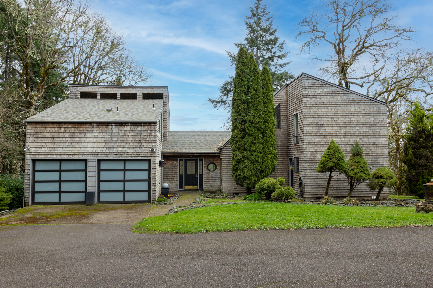Modern stone and wood house exterior with large garage doors and manicured lawn under blue sky.