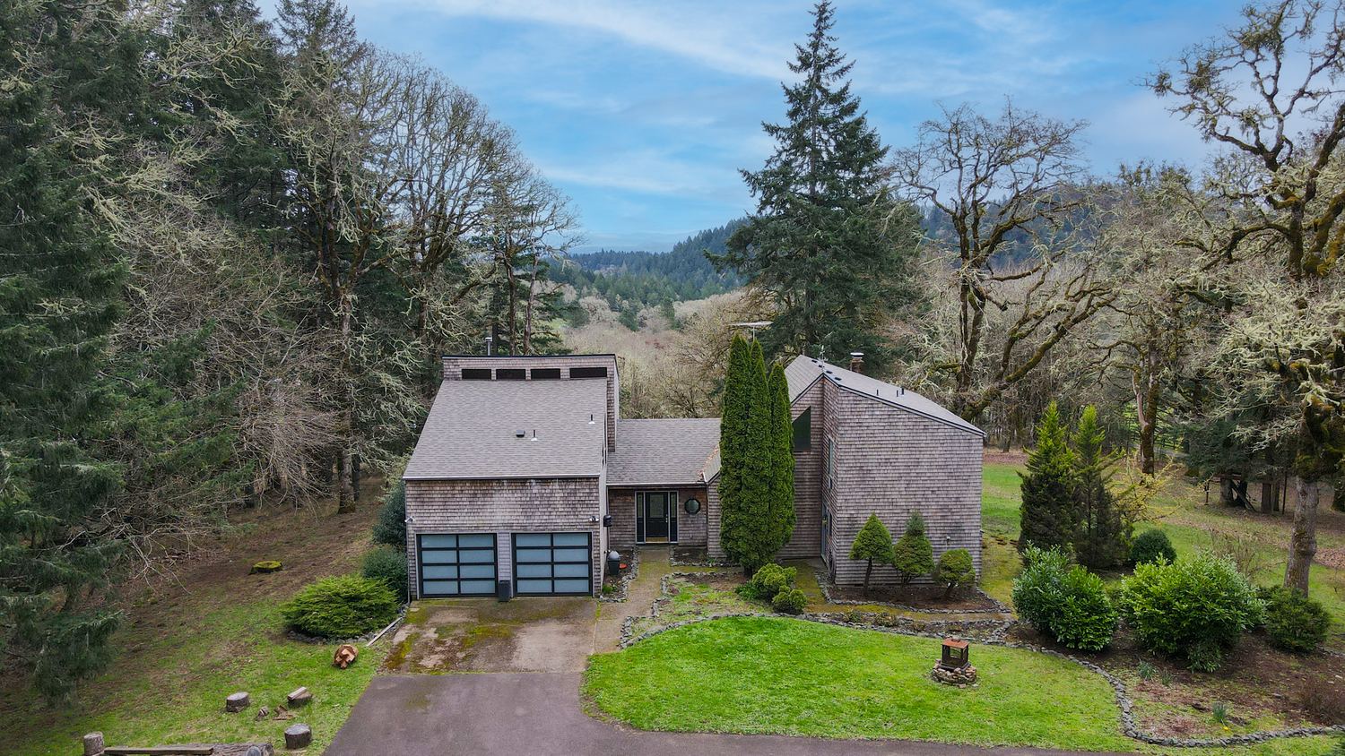 Scenic aerial view of a rural property with multiple outbuildings nestled among evergreen trees on a sunny day.