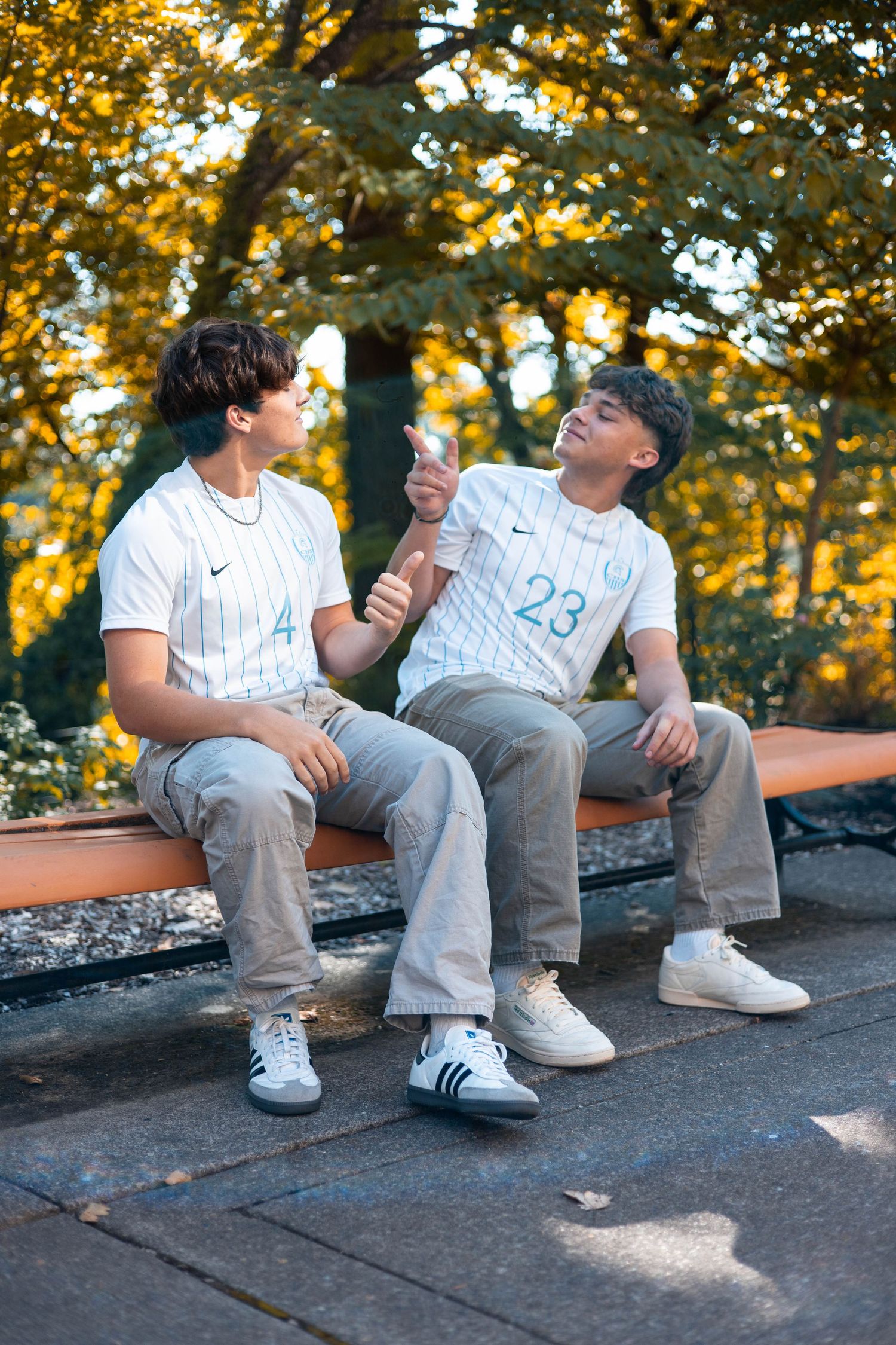 Two people sit on a stone wall sharing ice cream cones on a sunny autumn day with golden leaves in the background.