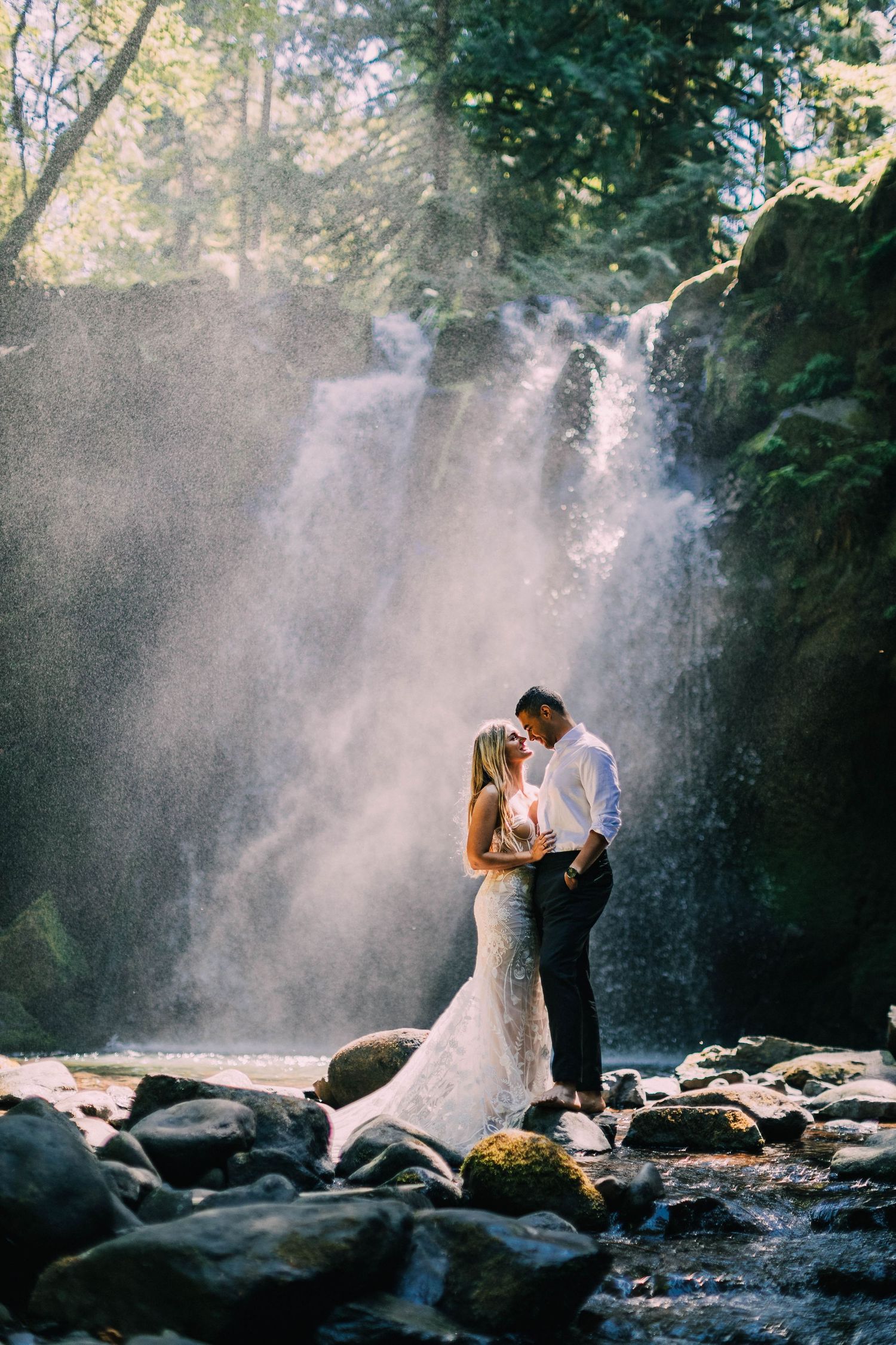 Romantic wedding portraits with cascading waterfall and sunlight creating ethereal atmosphere.