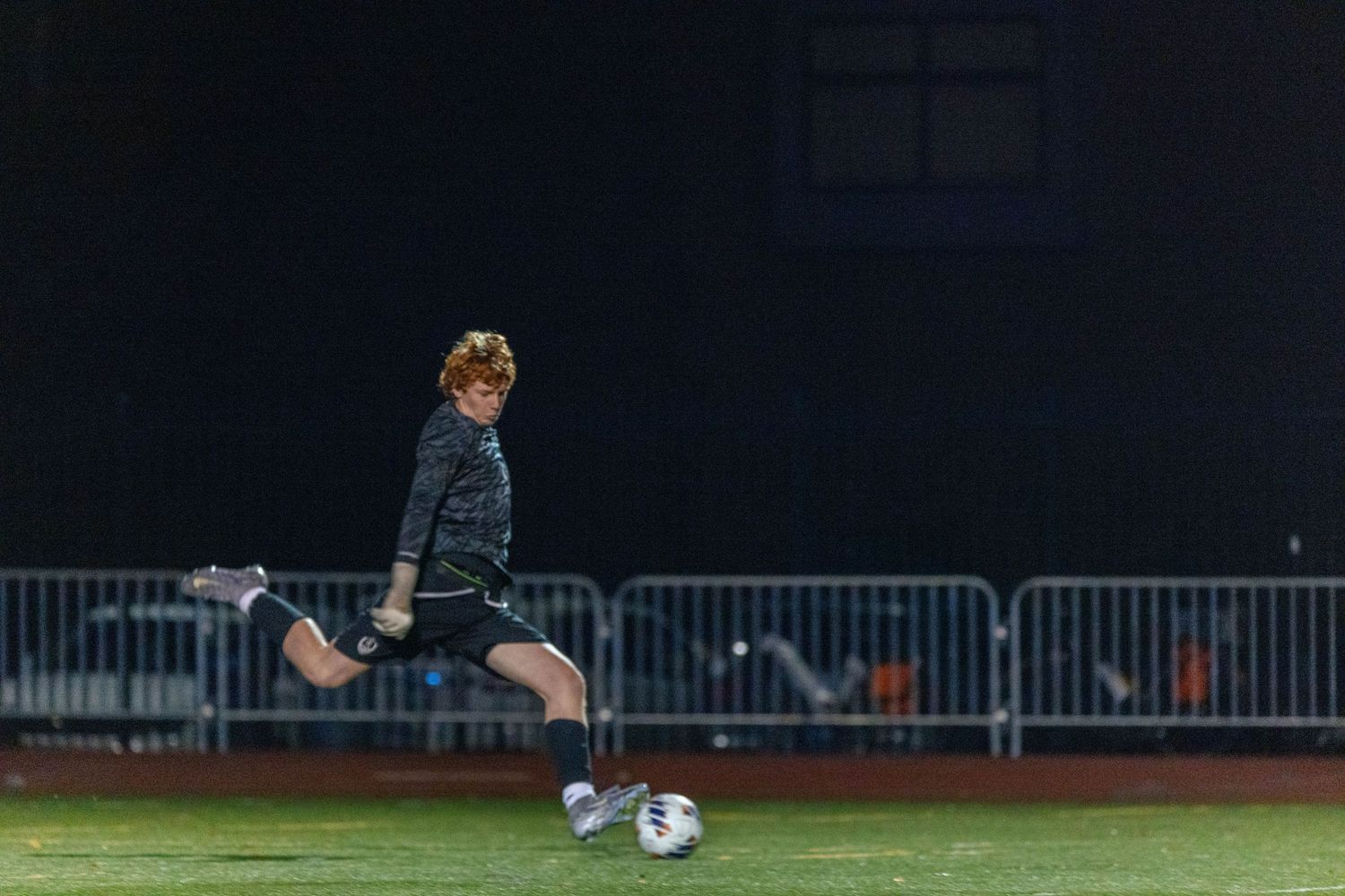 Soccer player performs a diving save on a grass field during nighttime match under stadium lights.