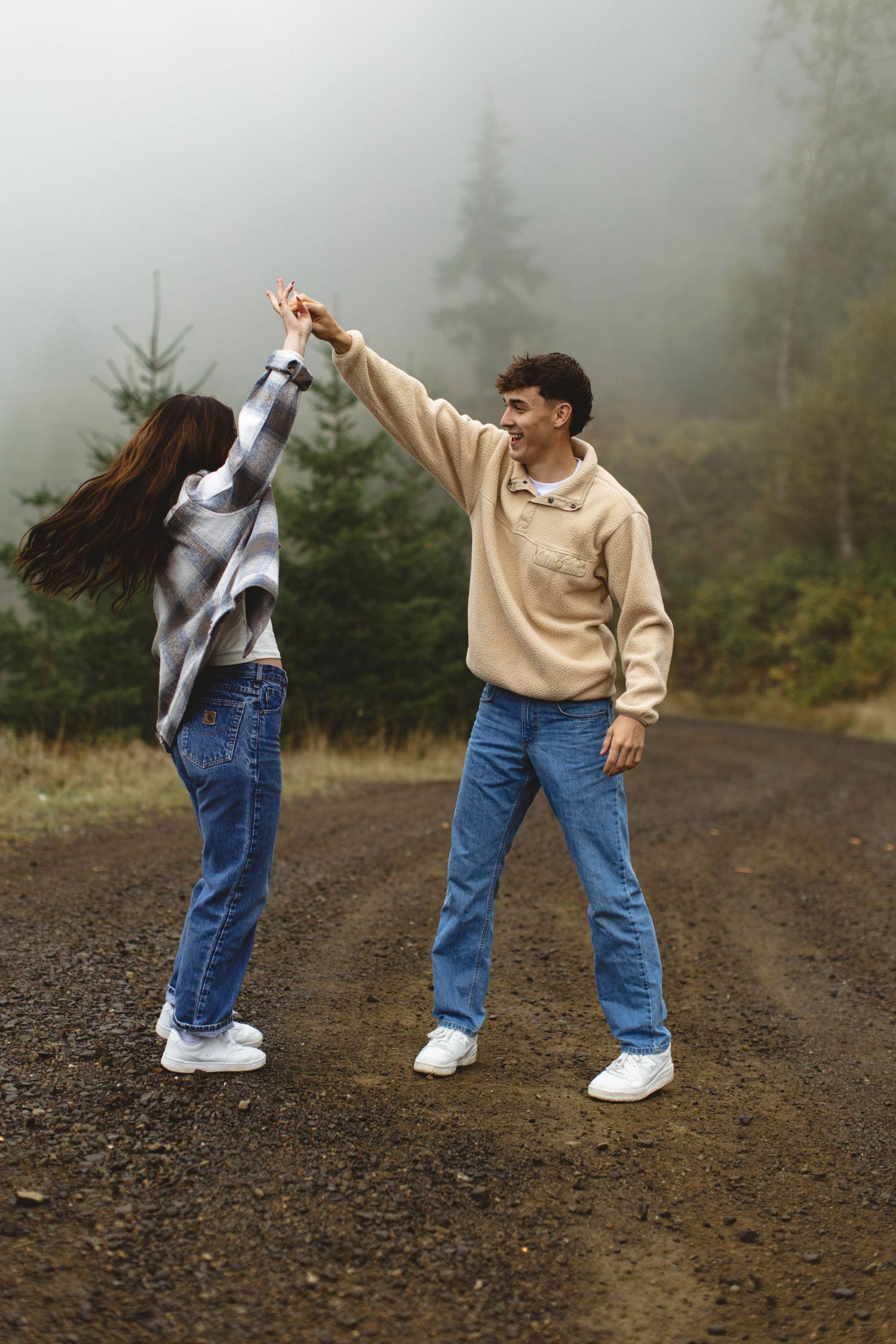 Person in beige sweater and jeans performs dynamic dance moves in a misty outdoor setting.