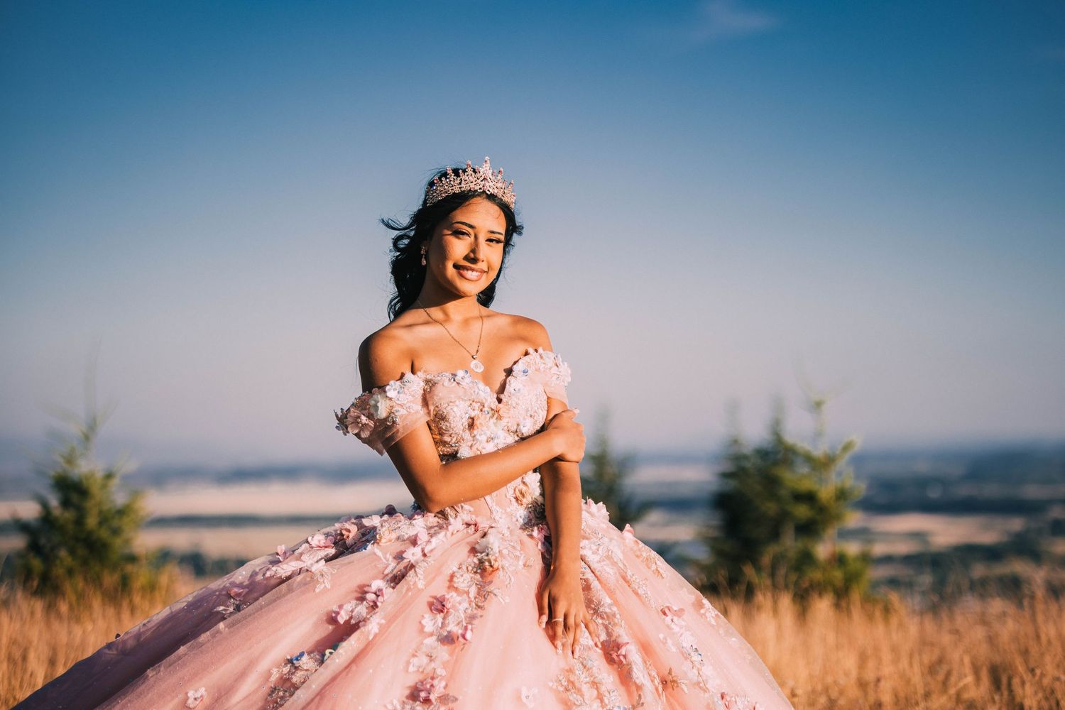A person in a pink floral gown poses gracefully in a golden field at sunset.