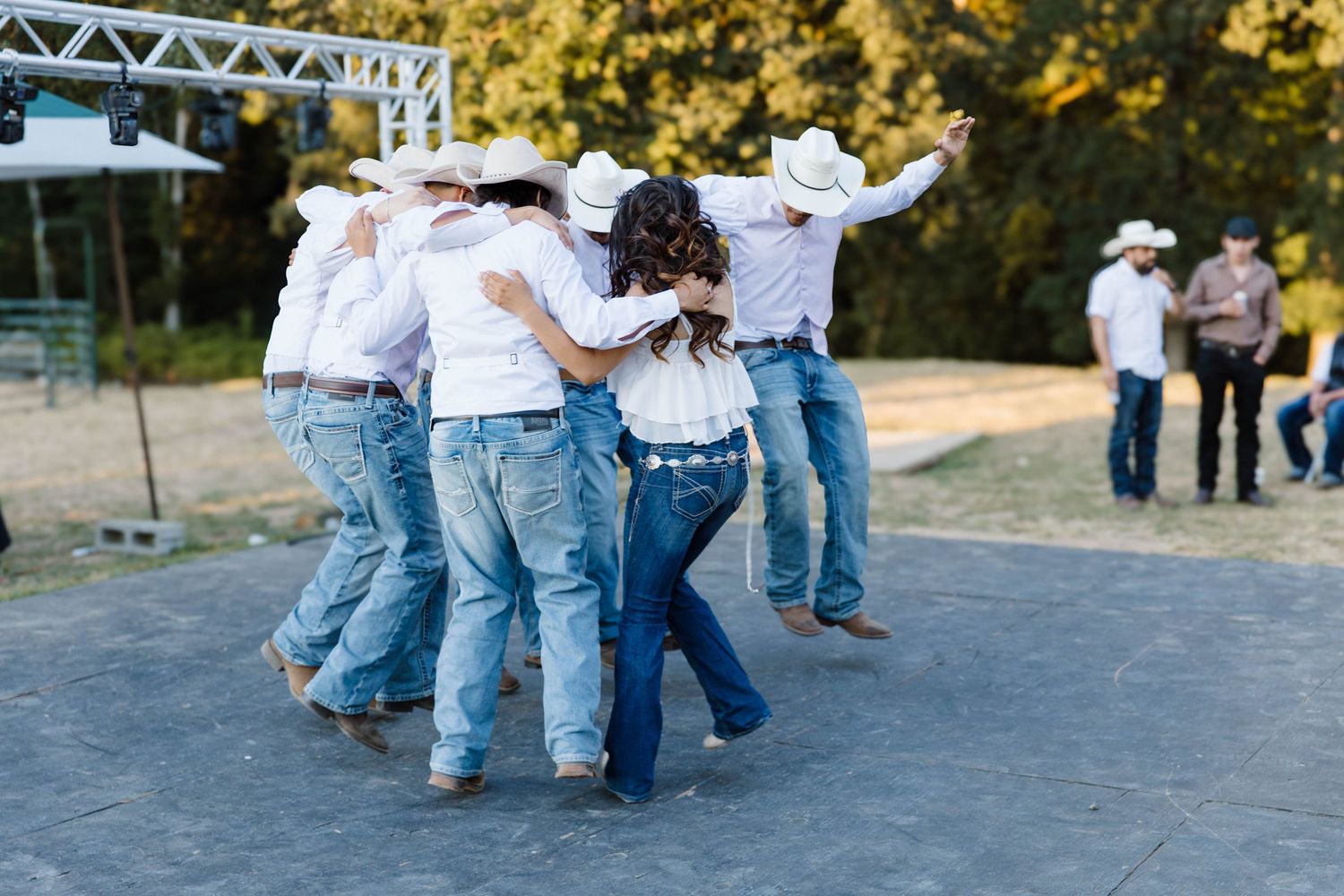 Dancers perform traditional line dancing moves on a paved outdoor area during a country western event.