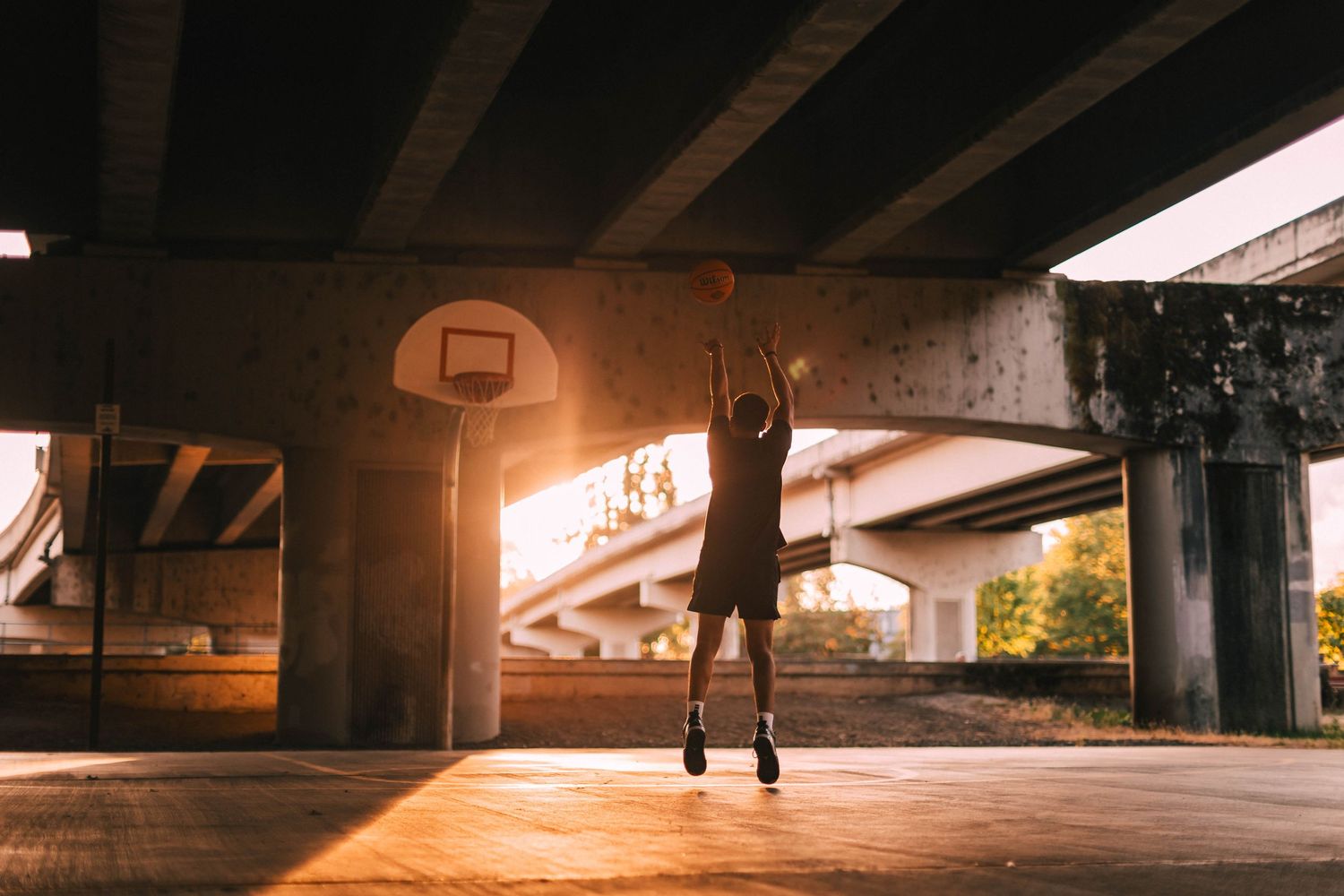 Dramatic low angle view under a concrete bridge or overpass illuminated by warm lighting at night.