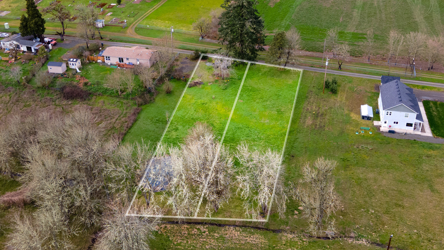 Aerial view of rural farmland with green fields, scattered trees, and residential properties in the countryside.