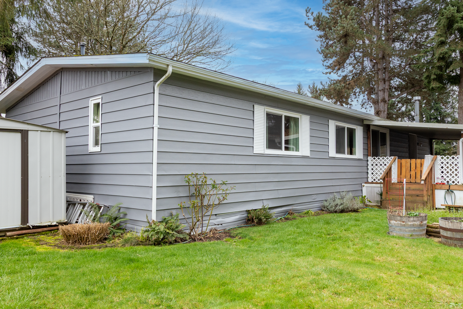 Gray ranch-style house with white trim sits on a sloping green lawn under blue skies.