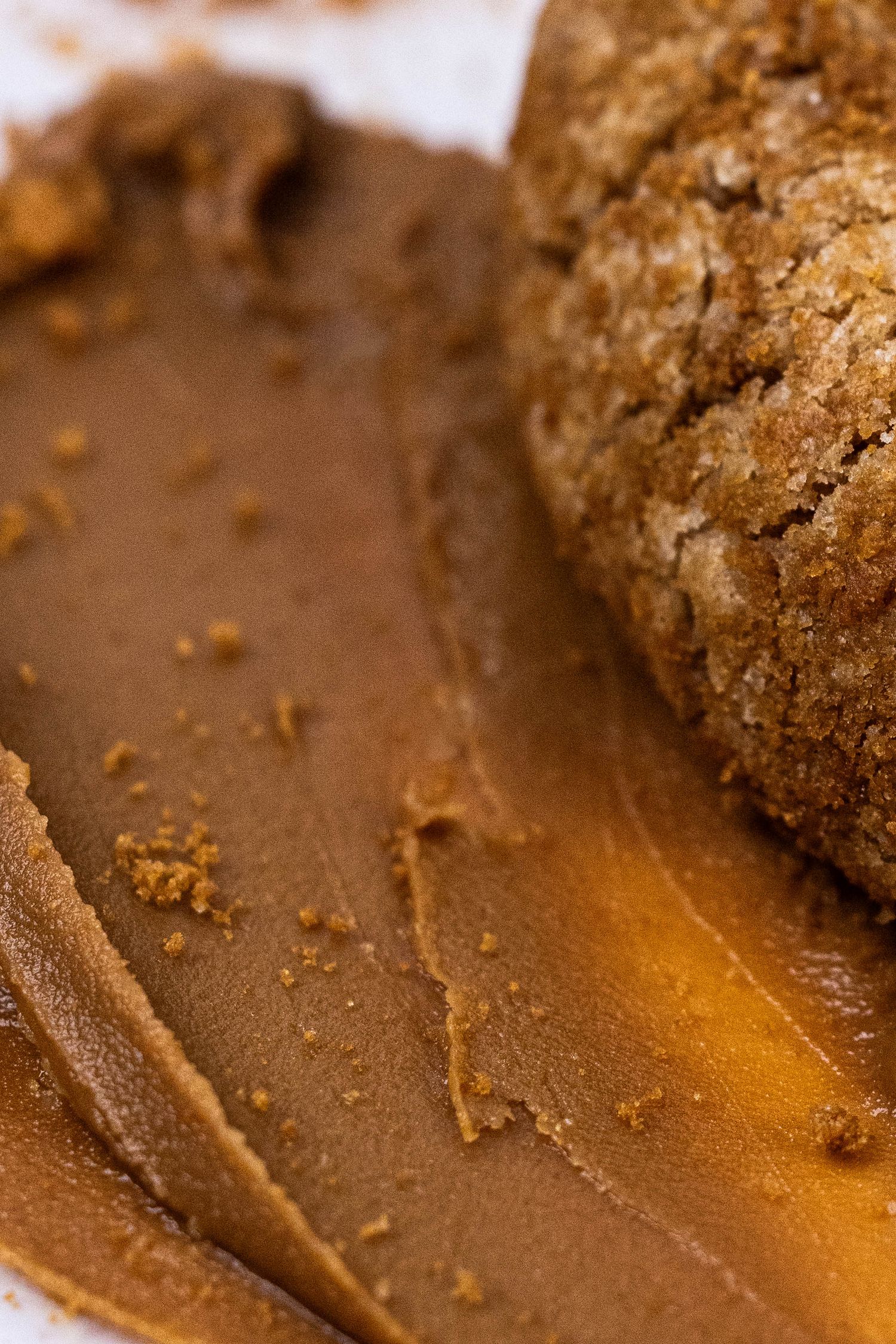 Close-up macro shot of chocolate cookie crumbs and melted caramel on a dark brown surface.