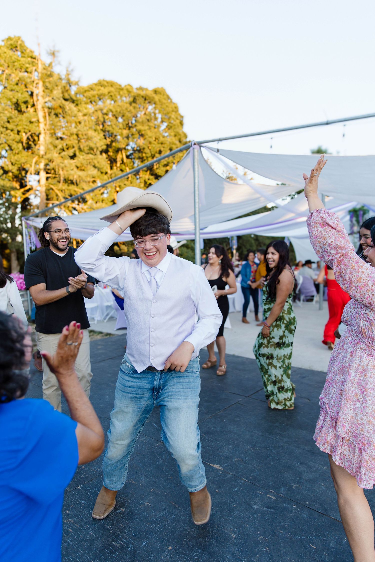 People dancing and having fun at an outdoor event with white tents and trees in the background.