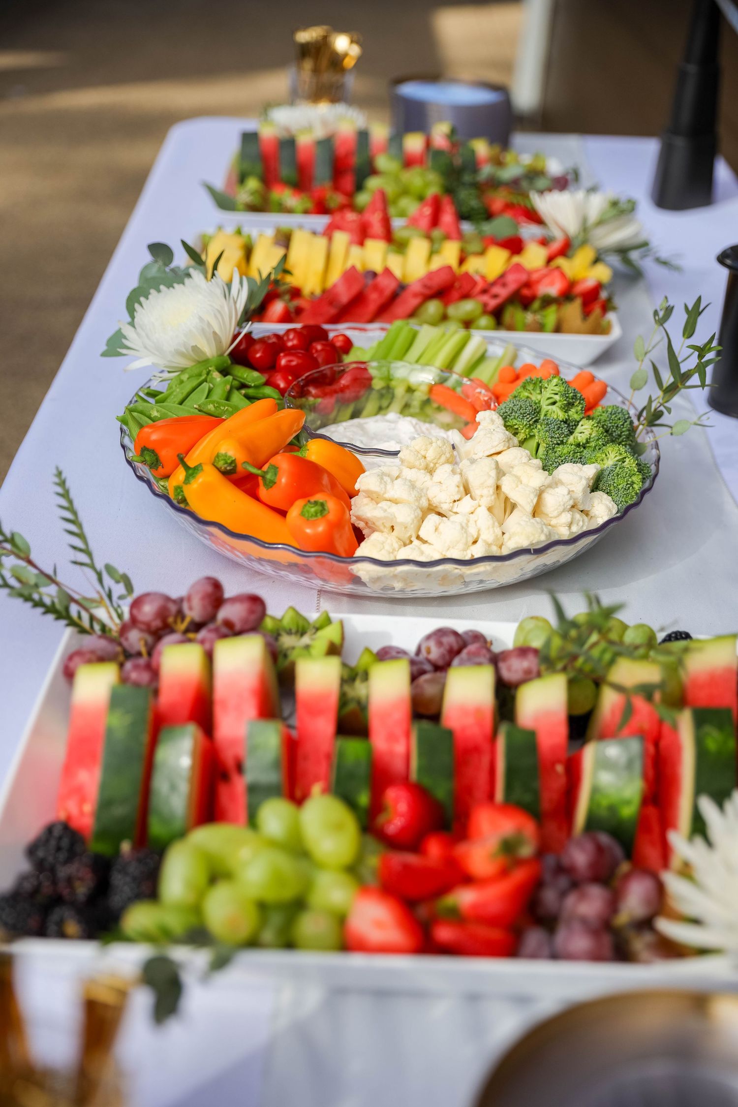 Fresh vegetable and fruit platters with colorful bell peppers, grapes, tomatoes, and cucumbers arranged for a party spread.