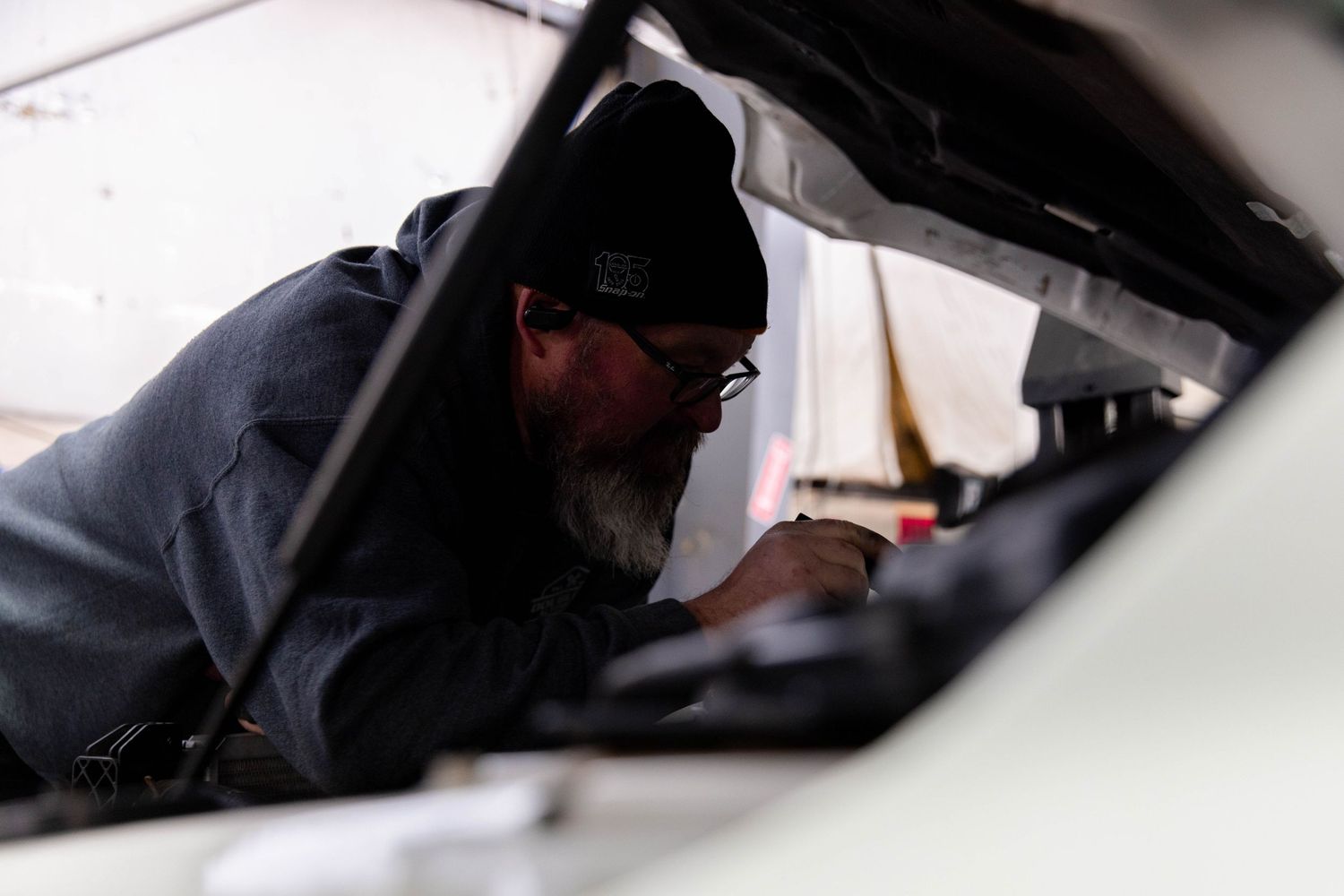 A close-up view of a mechanic performing maintenance work under a car hood in a repair shop.