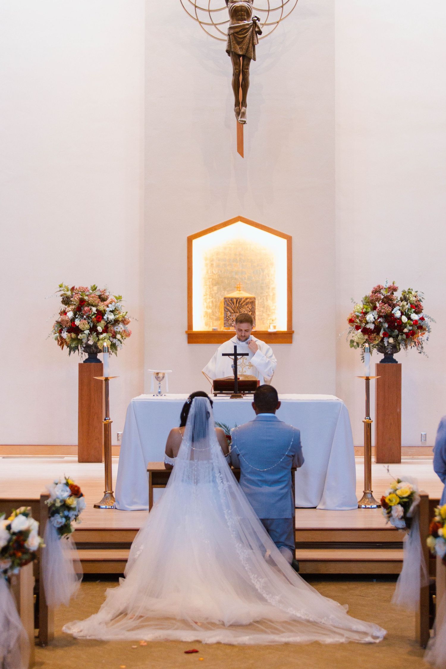 A couple kneels at the altar during their wedding ceremony in a minimalist white church interior.