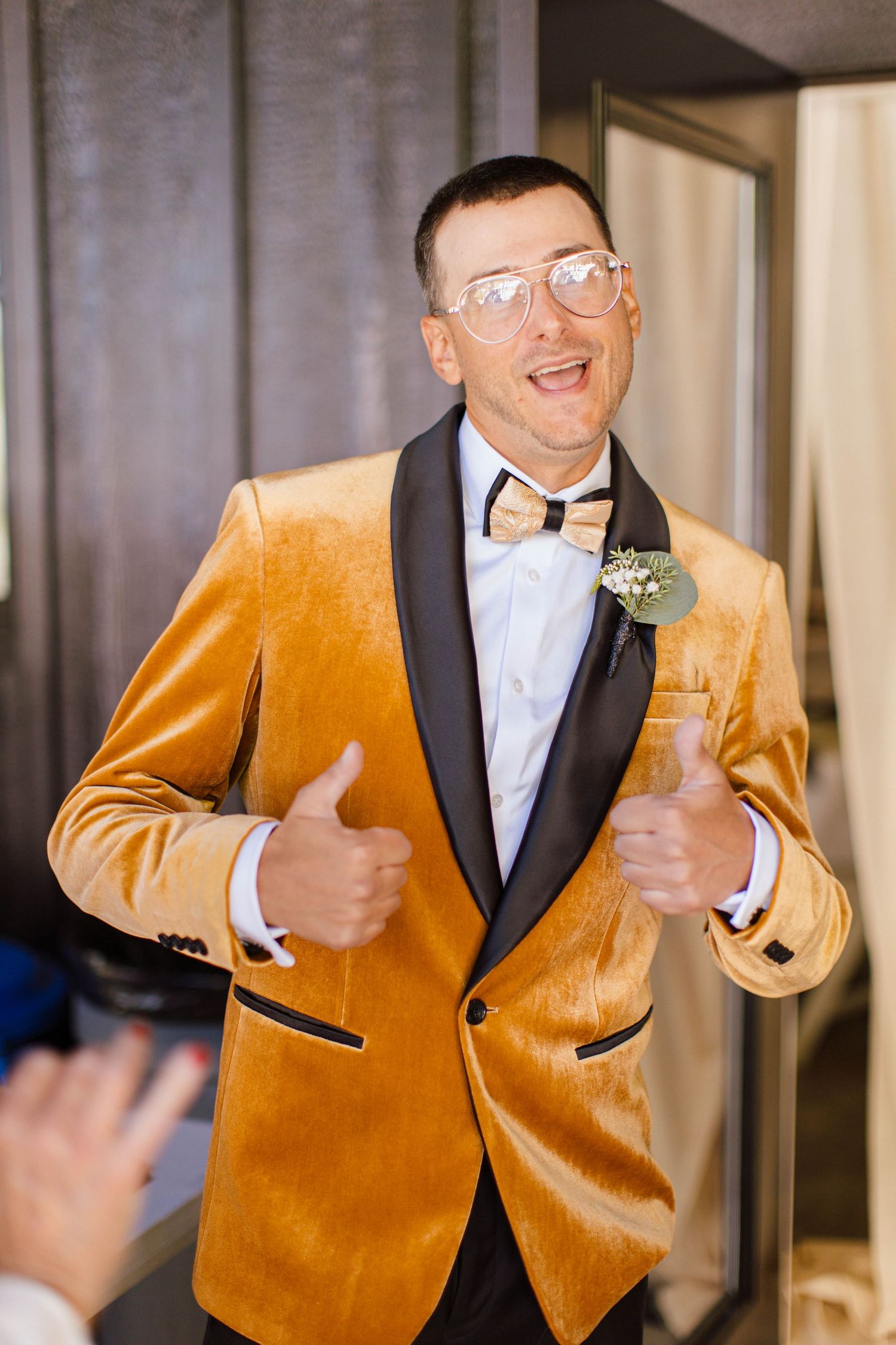 Person in a gold velvet tuxedo jacket and black bow tie gives thumbs up gesture with a cheerful expression.