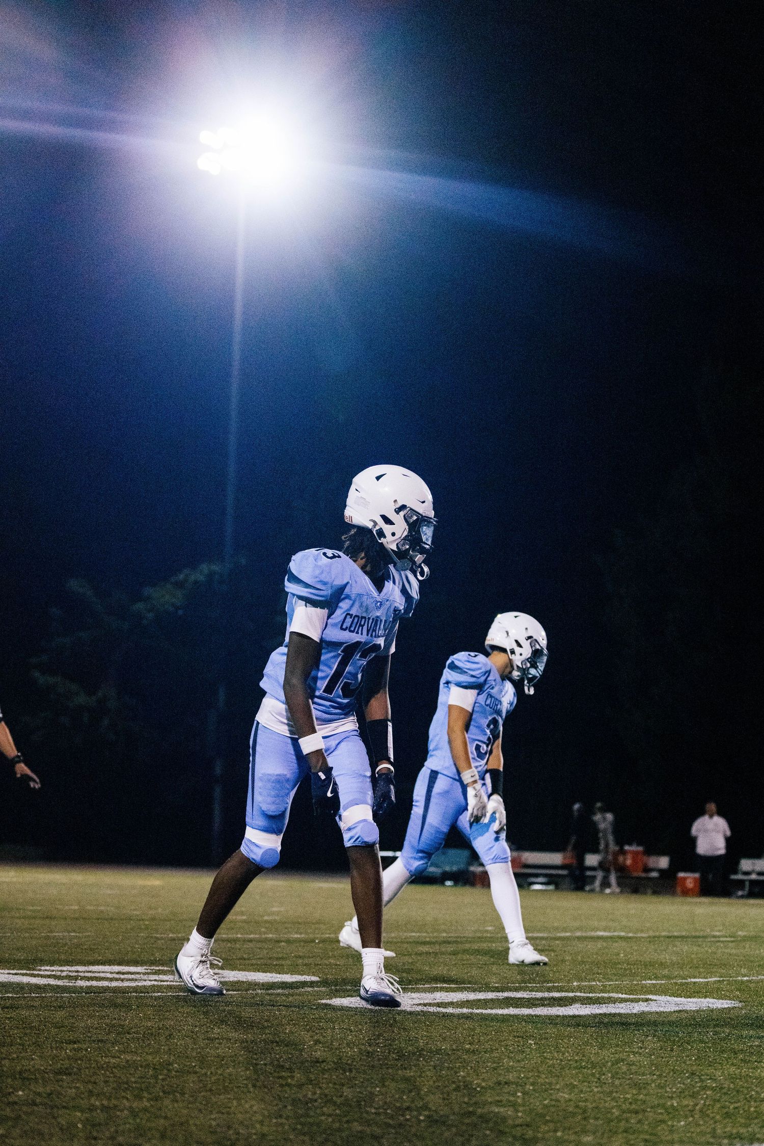Football players line up in formation on a nighttime field under bright stadium lights during a game.