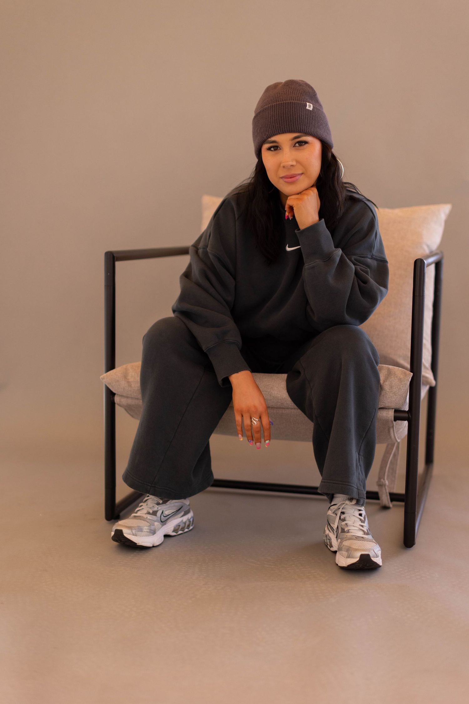 A person in dark clothing and beanie sits on a bench in various casual poses against a neutral background.