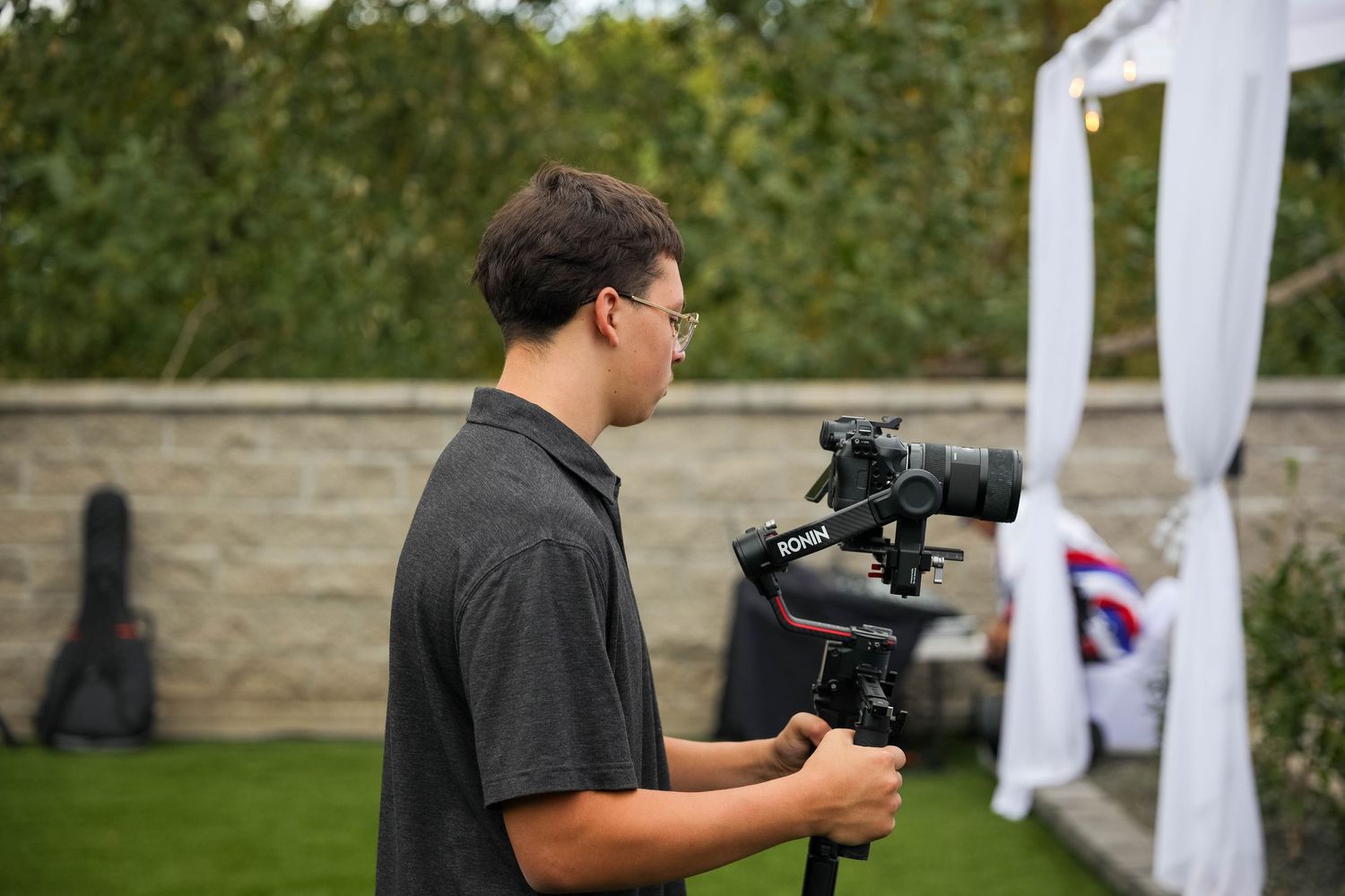 Professional videographer shooting footage in garden setting with white drapes in background.