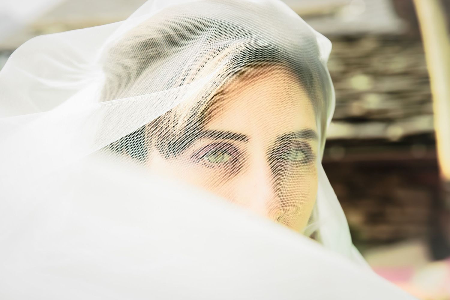 Photo portrait de la mariée Angélique et son voile devant son visage, mise en valeur de son regard à Séez Ferme d'Angèle,