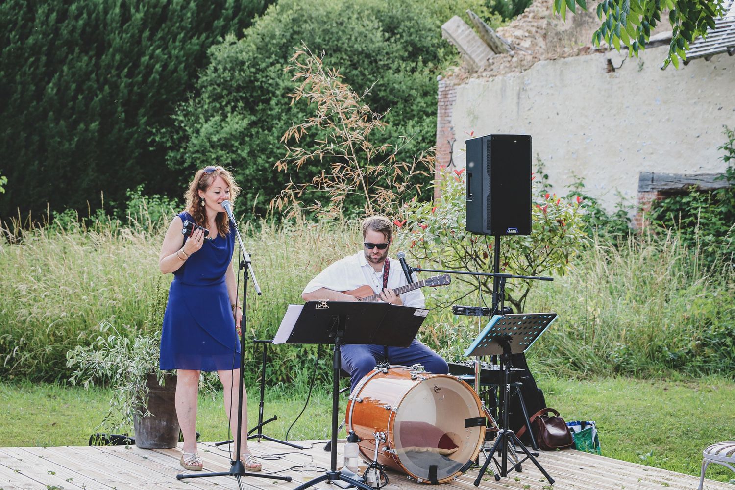 Artiste chantant en robe bleue accompagnée d’un batteur lors d’un mariage en extérieur, ambiance musicale et conviviale dans un jardin