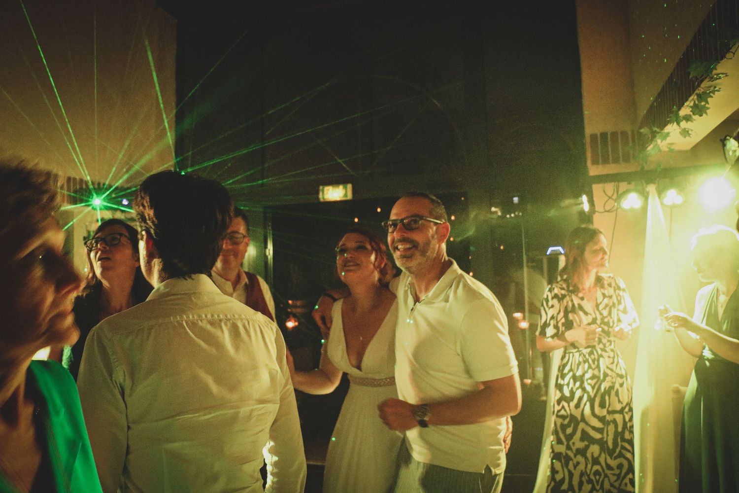 Invités dansant lors d'une réception de mariage avec des jeux de lumières laser verts et une ambiance festive de soirée.