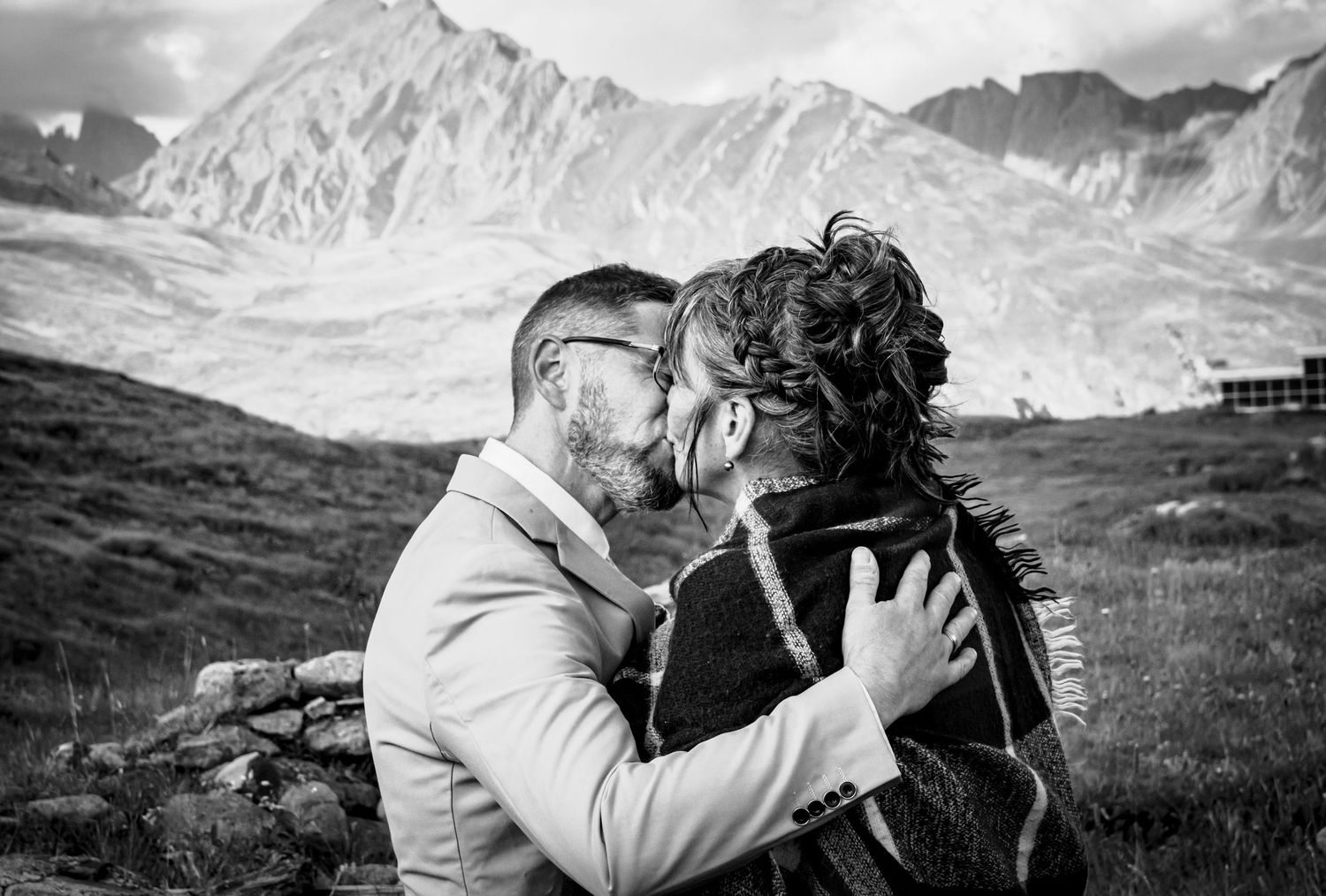 Couple de mariés s'embrassant tendrement élégants devant un paysage montagnard spectaculaire, ambiance romantique et intemporelle