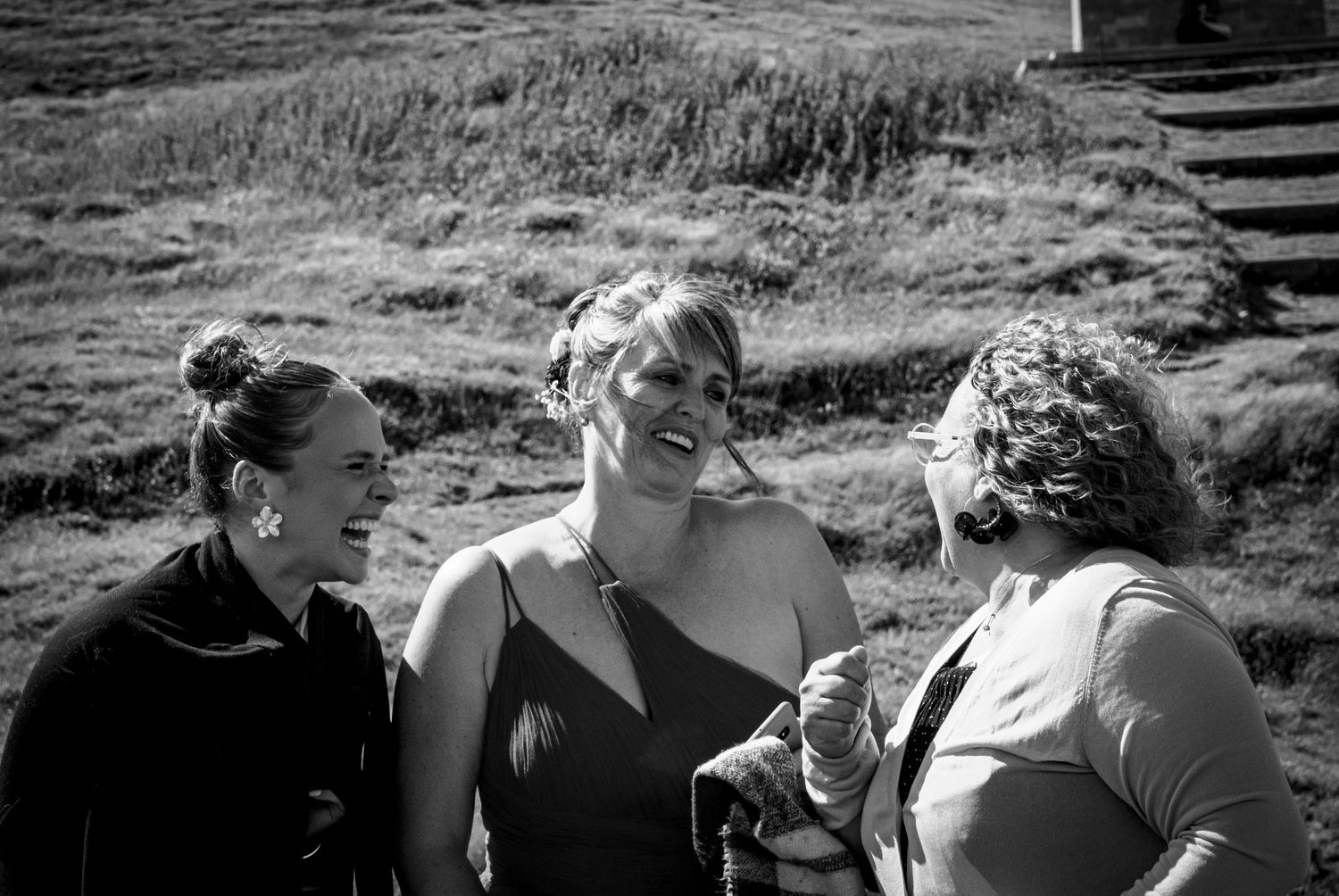 Mariée rayonnante entourée de sa fille et d'une invitée, moment de complicité et de rire lors d'un mariage en extérieur, ambiance naturelle