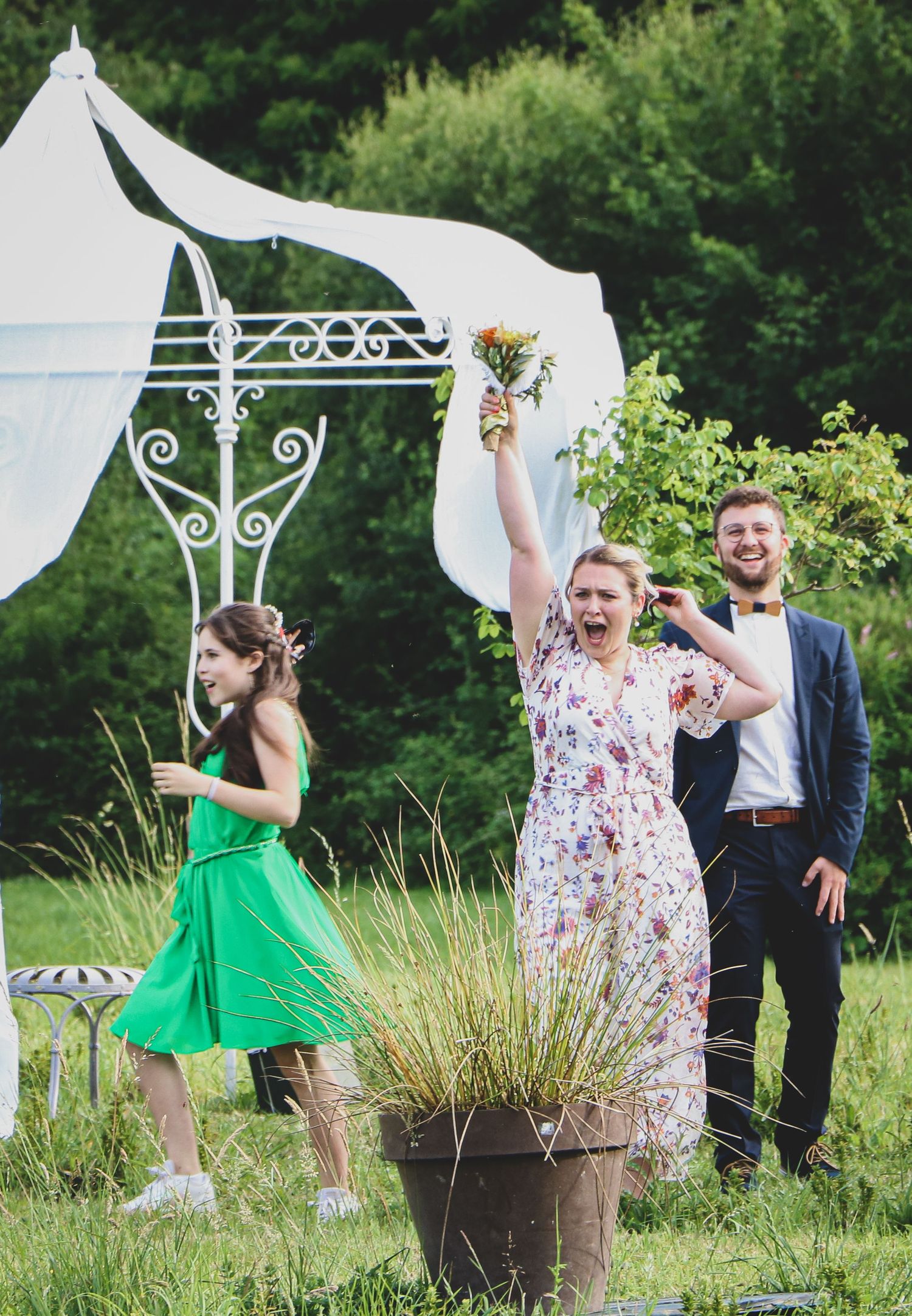 La soeur de la mariée à trouvé le bouquet de la mariée sous une arche décorée lors d’une cérémonie en extérieur, mariage ambiance champêtre.