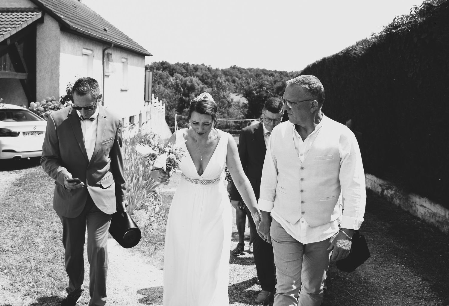 Mariée émue marchant main dans la main avec son père dans un jardin après la cérémonie, ambiance intimiste et touchante en noir et blanc