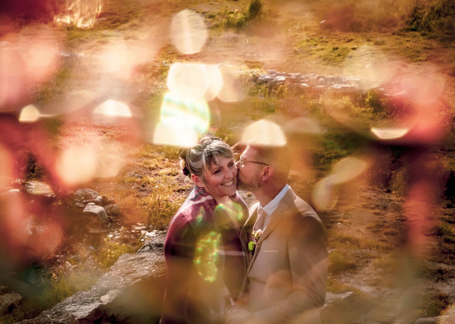 Photo des mariés Aurélie et Johnny au col du Petit Saint Bernard, photo prise à travers un bijoux qui entoure de jolis reflets les mariés