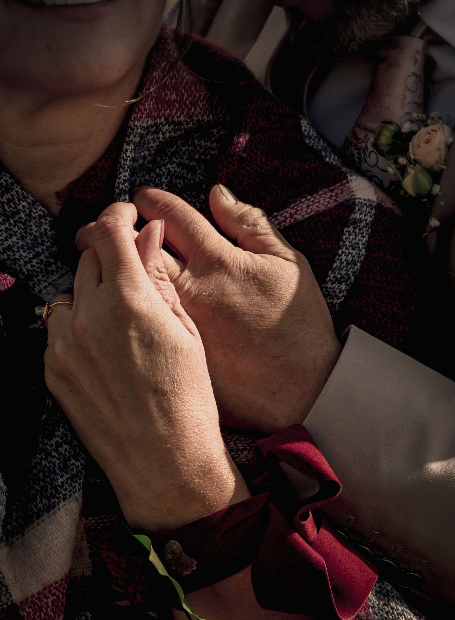 Gros plan sur les mains entrelacées d'un couple de mariés, détail des alliances et du plaid tartan, ambiance chaleureuse et romantique.