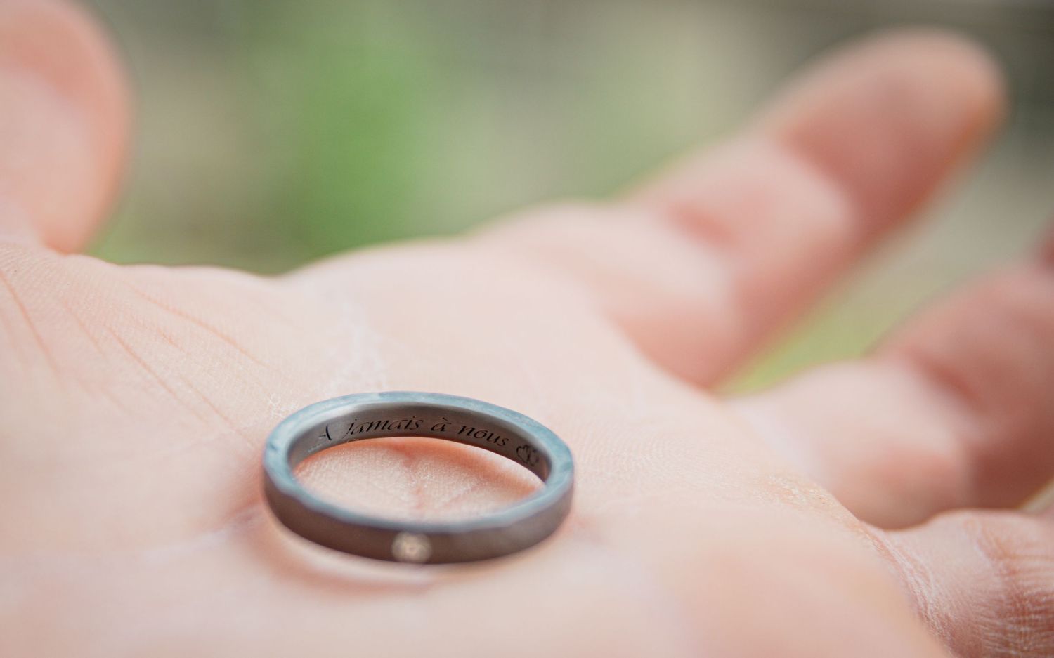 Gros plan d'une alliance fine posée dans la paume d'une main, bague de mariage avec gravure intérieure personnalisée et petit diamant