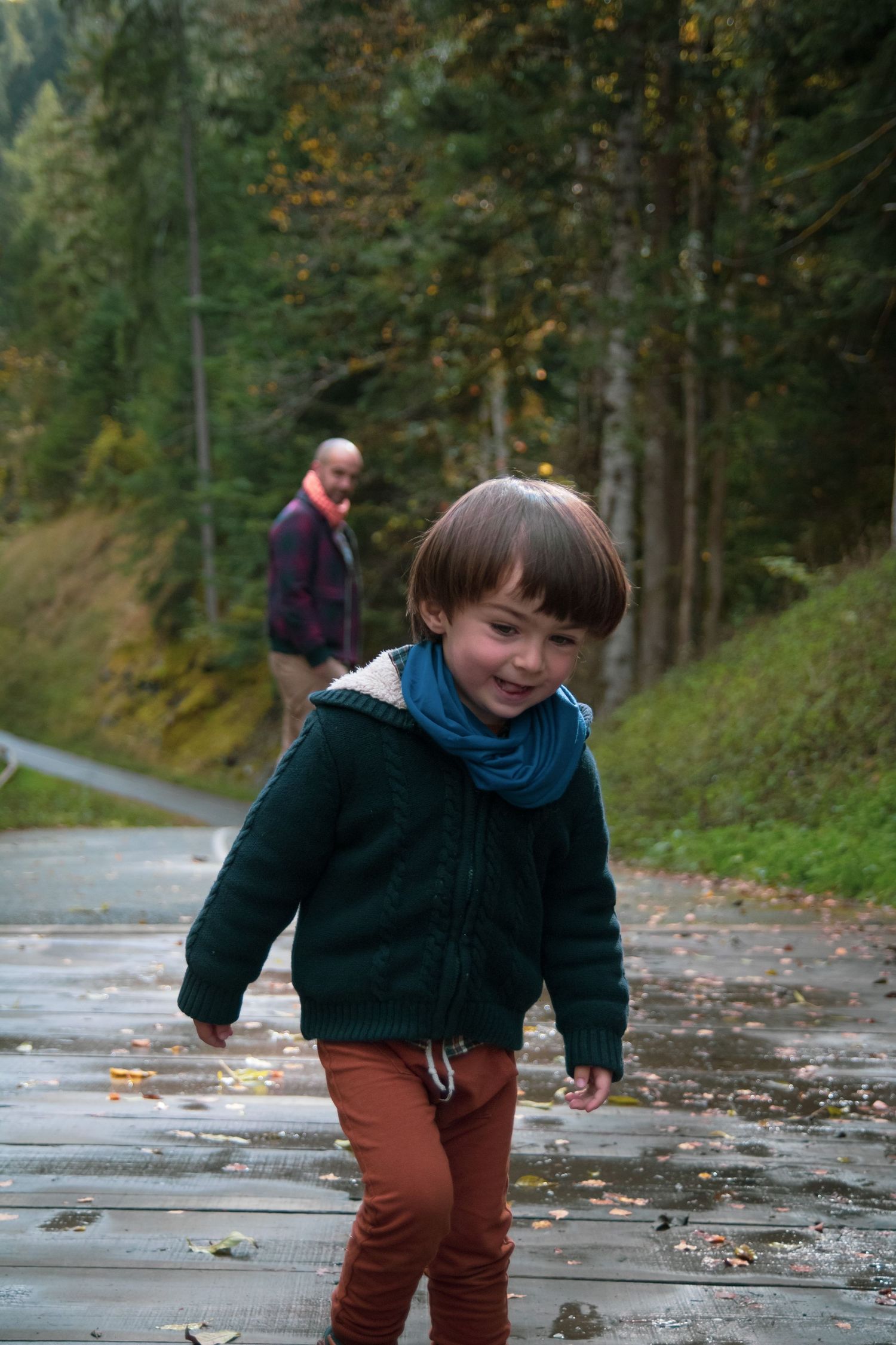Photo famille  d'un enfant avec son papa, qui joue avec les flaques d'eau à travers une fôret en automne, douce lumière par Alicia Casanova