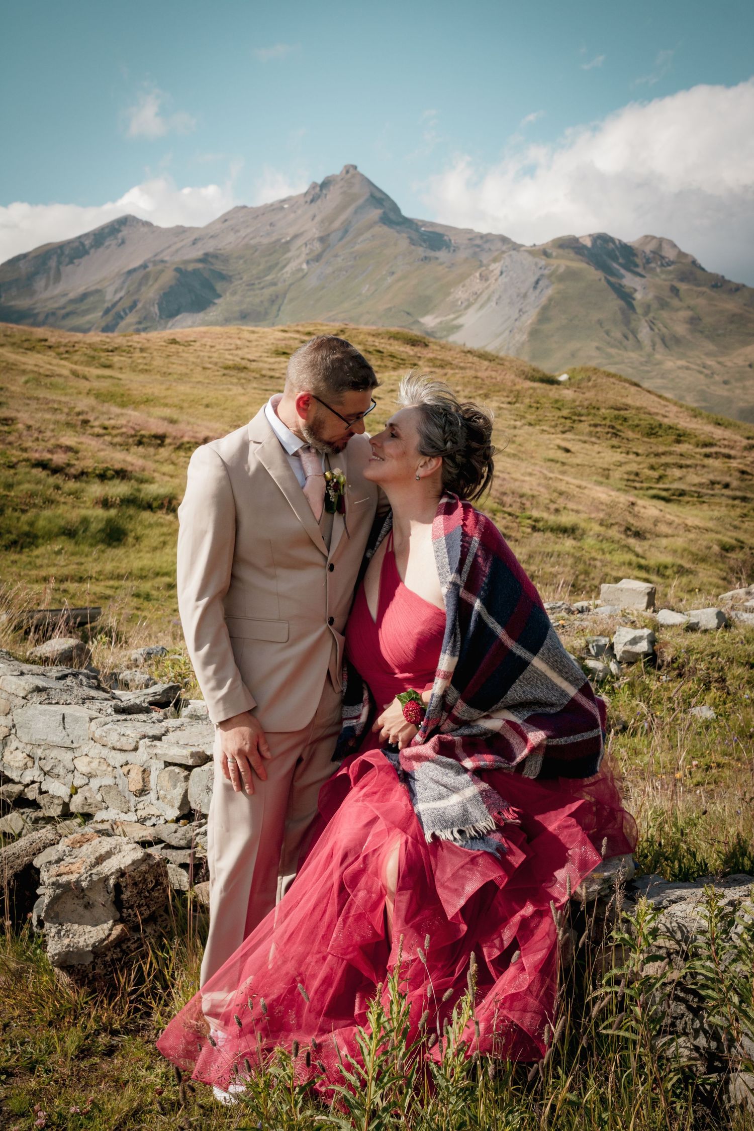 Couple mariés en montagne Savoie - Séance photo romantique par Alicia Casanova, robe rouge et costume beige, paysages alpins