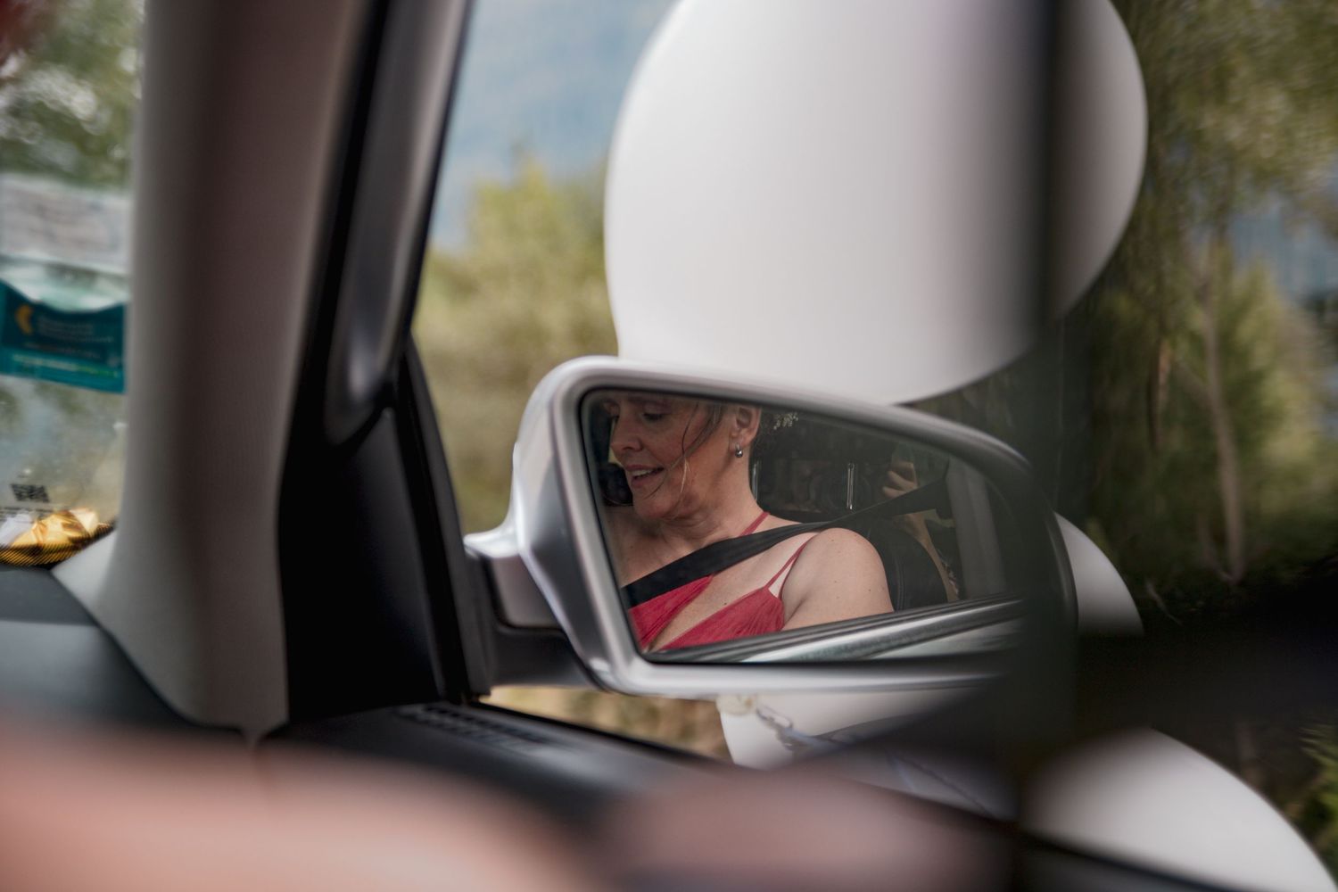 Mariée souriante se préparant pour son mariage, reflet dans le rétroviseur d'une voiture, ambiance intimiste et naturelle avant la cérémonie