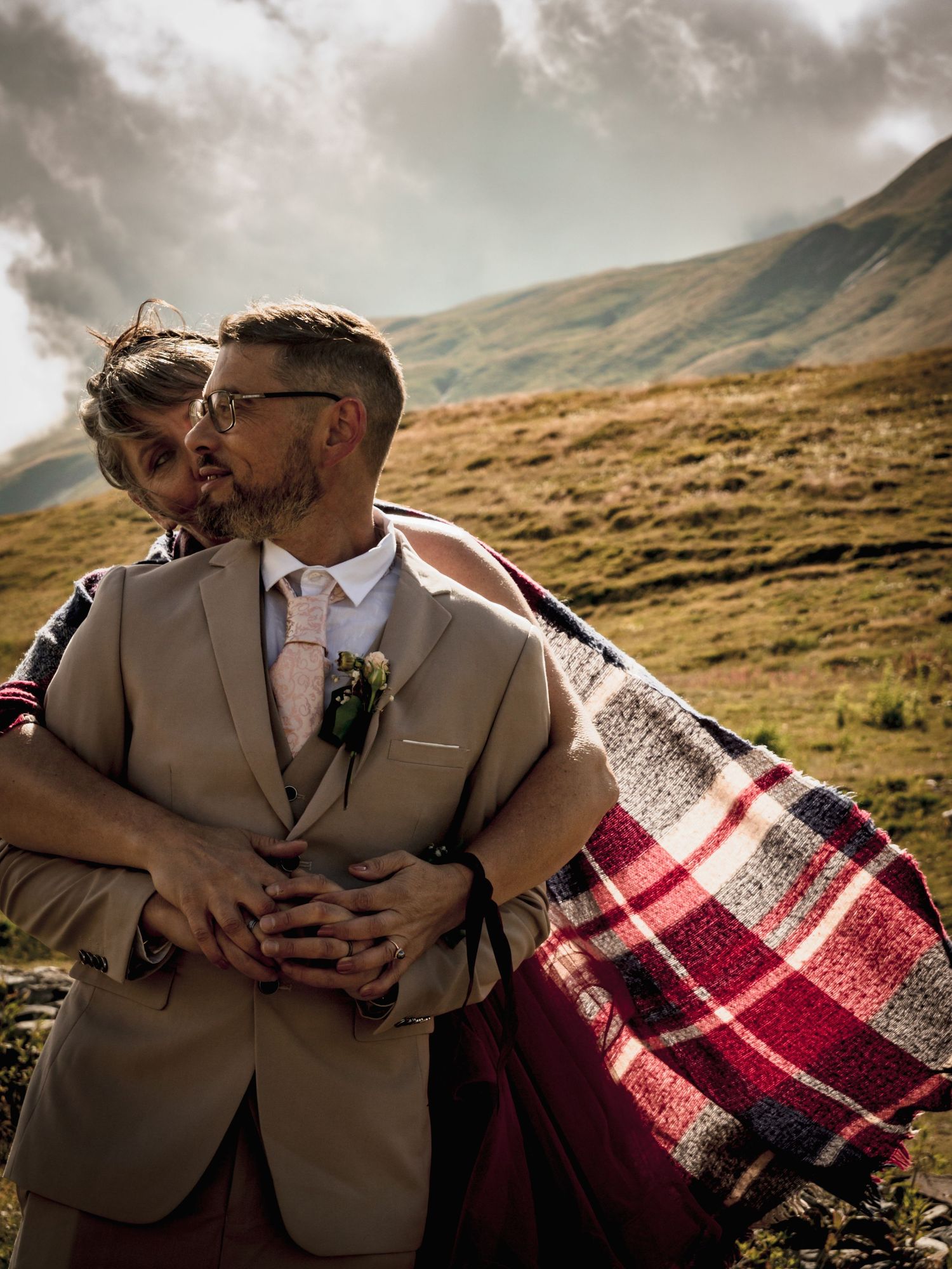 Mariée enlaçant son époux  en montagne Savoie - Séance photo mariage Alicia Casanova, costume beige et plaid, paysages grandioses