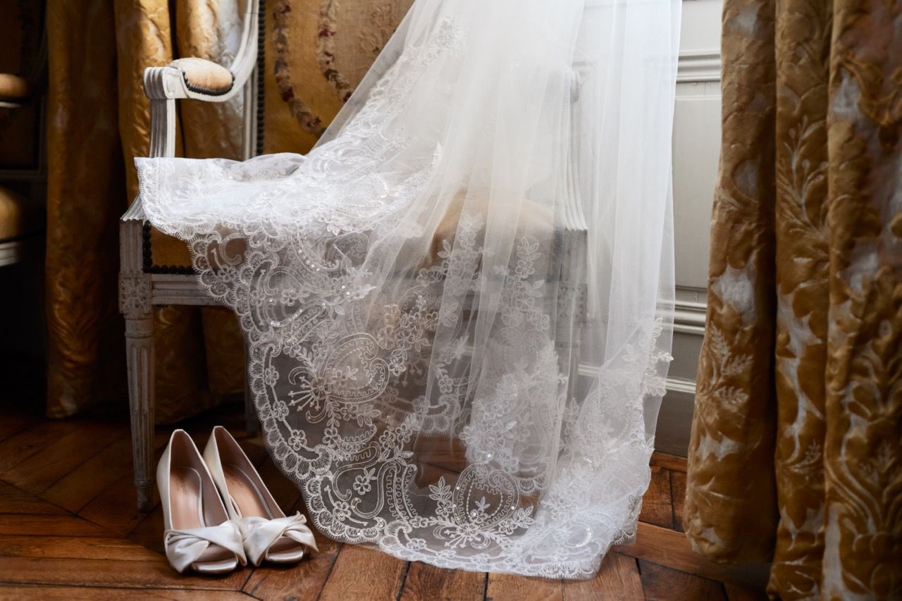 A delicate lace wedding veil and white bridal shoes arranged on a wooden floor.