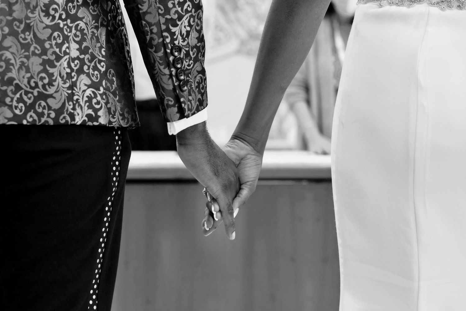 A black and white image showing two hands joined together with a wedding ring visible.