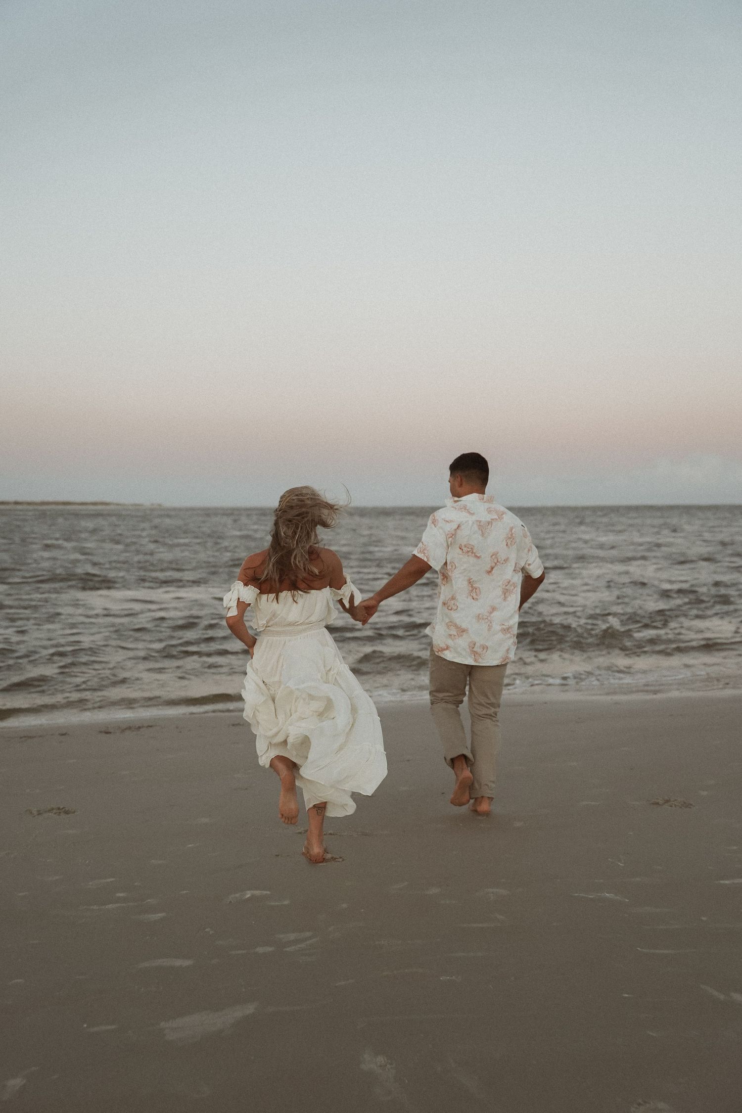 Couple walking hand in hand along the beach during a relaxed coastal photo session.
