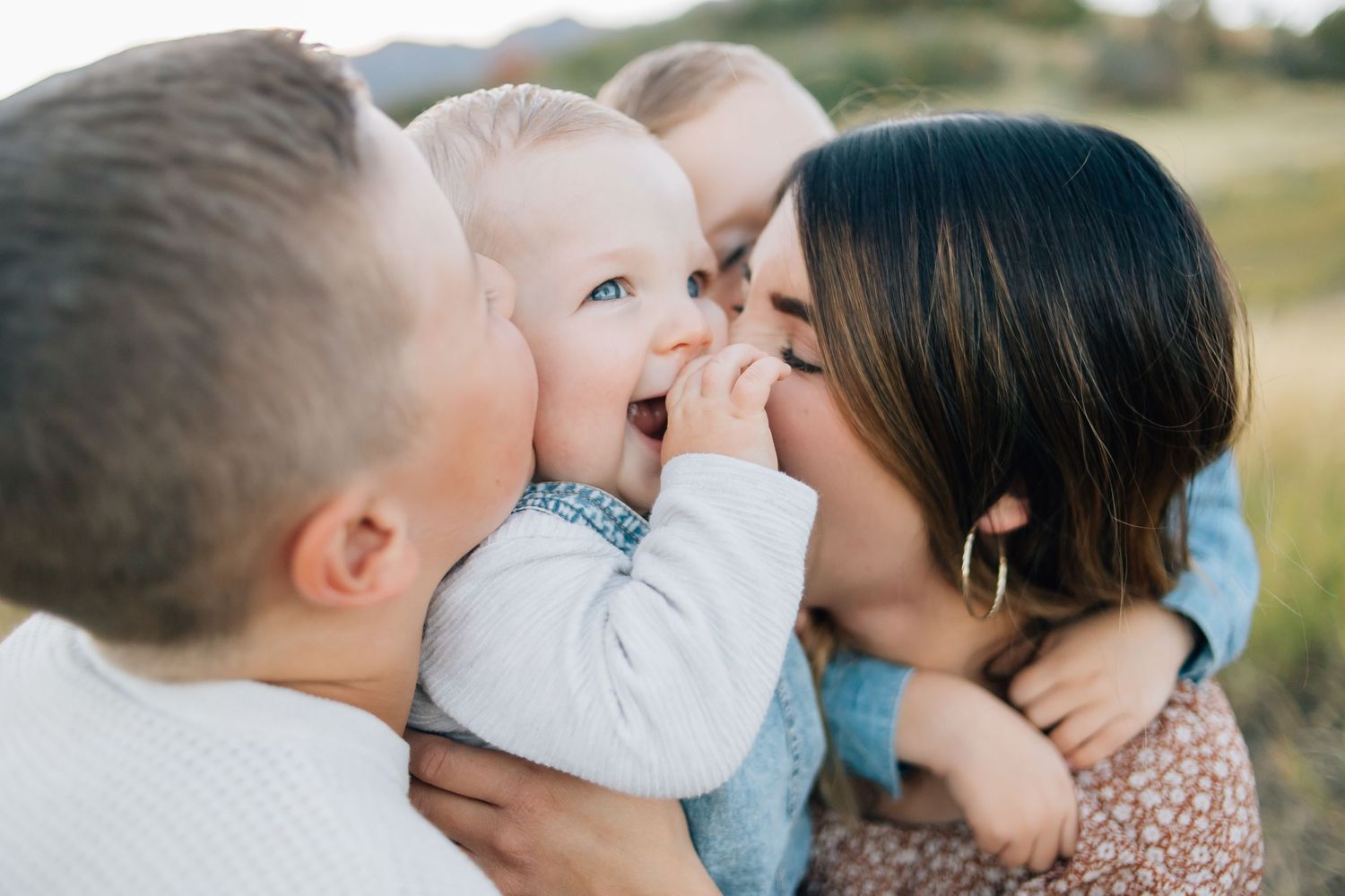 A family kissing their baby during a candid family photo shoot during natural light in the mountains