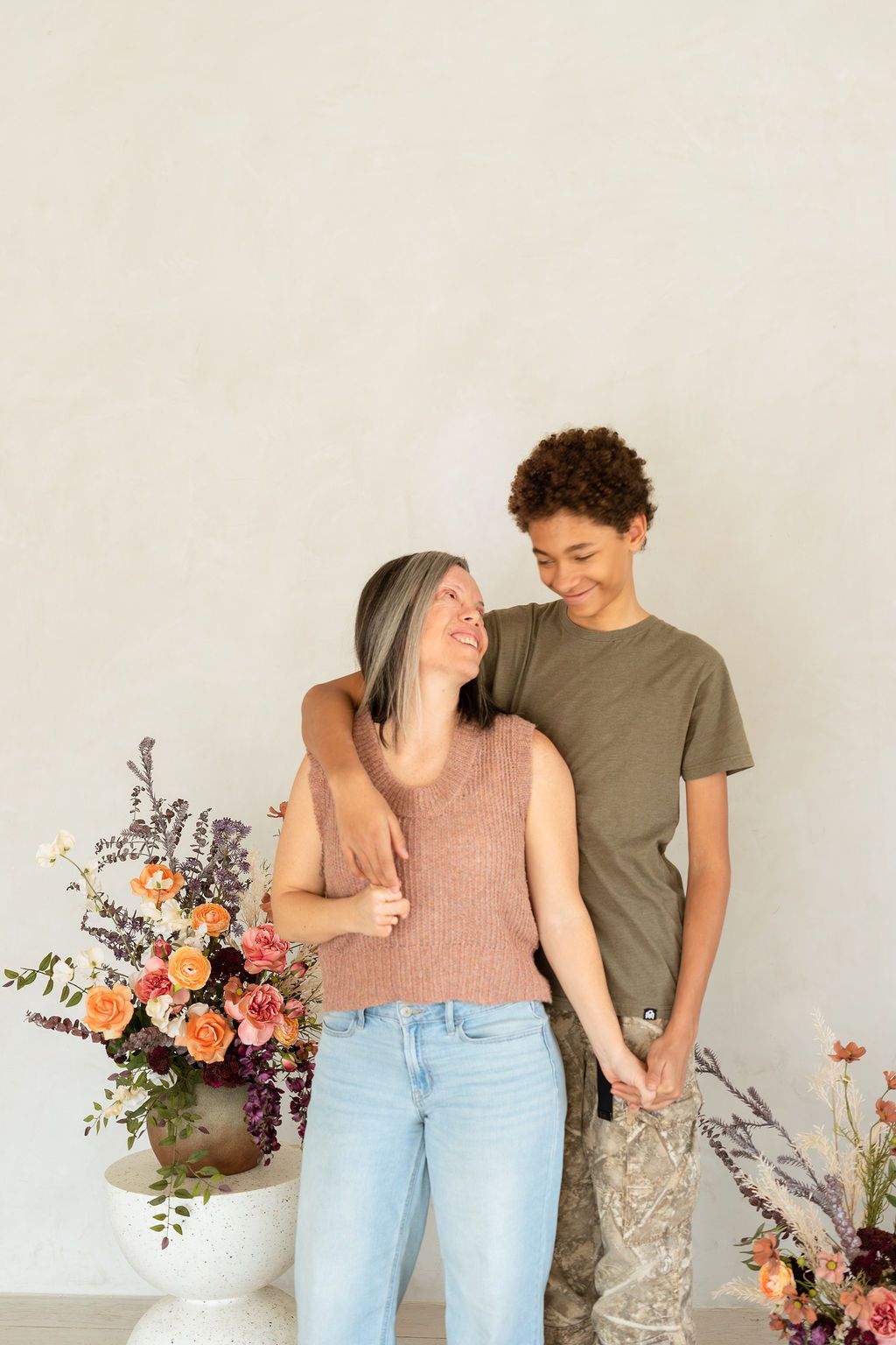 A mom and her teenaged son laughing together during an indoor photoshoot celebrating mother's day