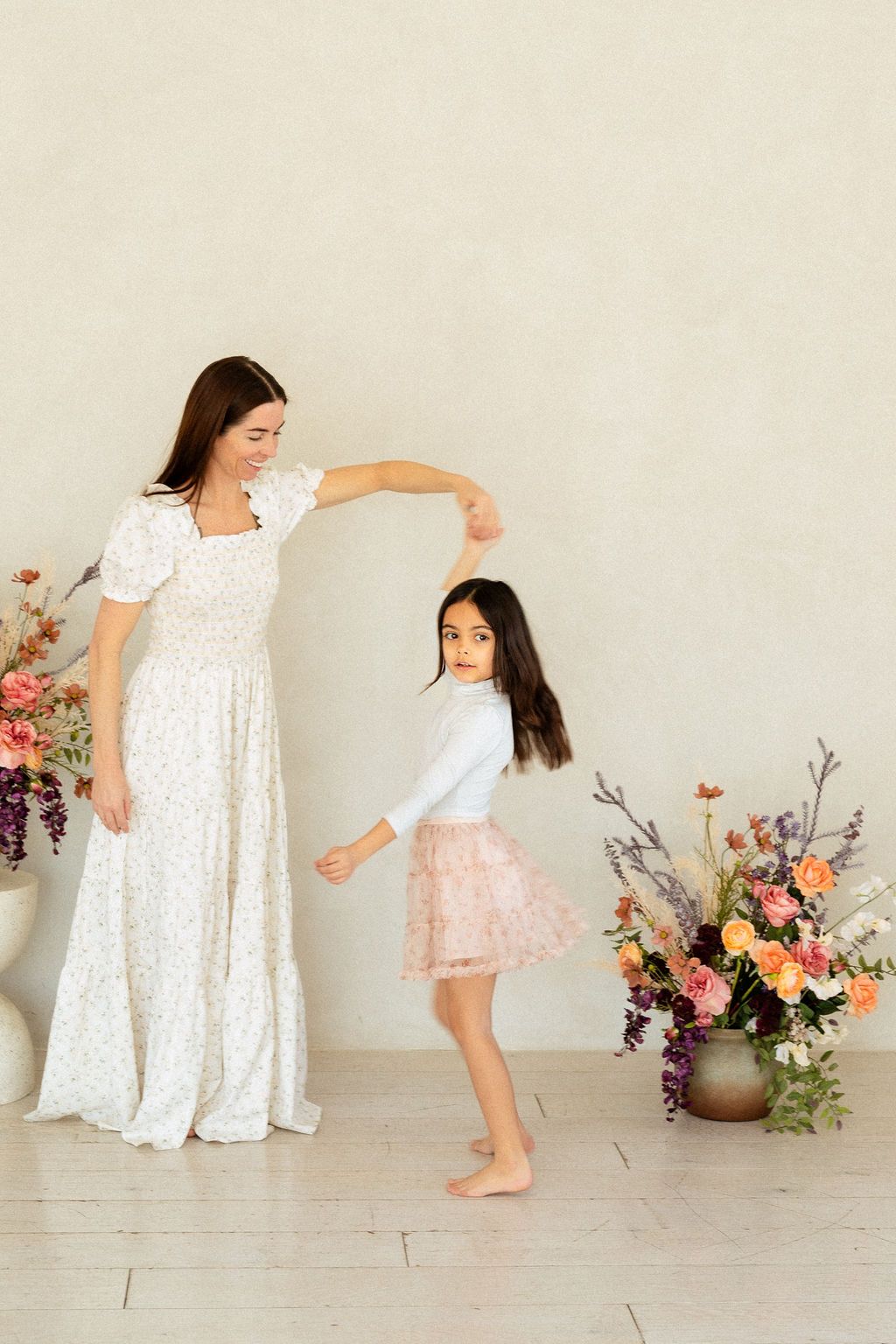 Mother and young daughter dancing during an indoor photoshoot celebrating motherhood
