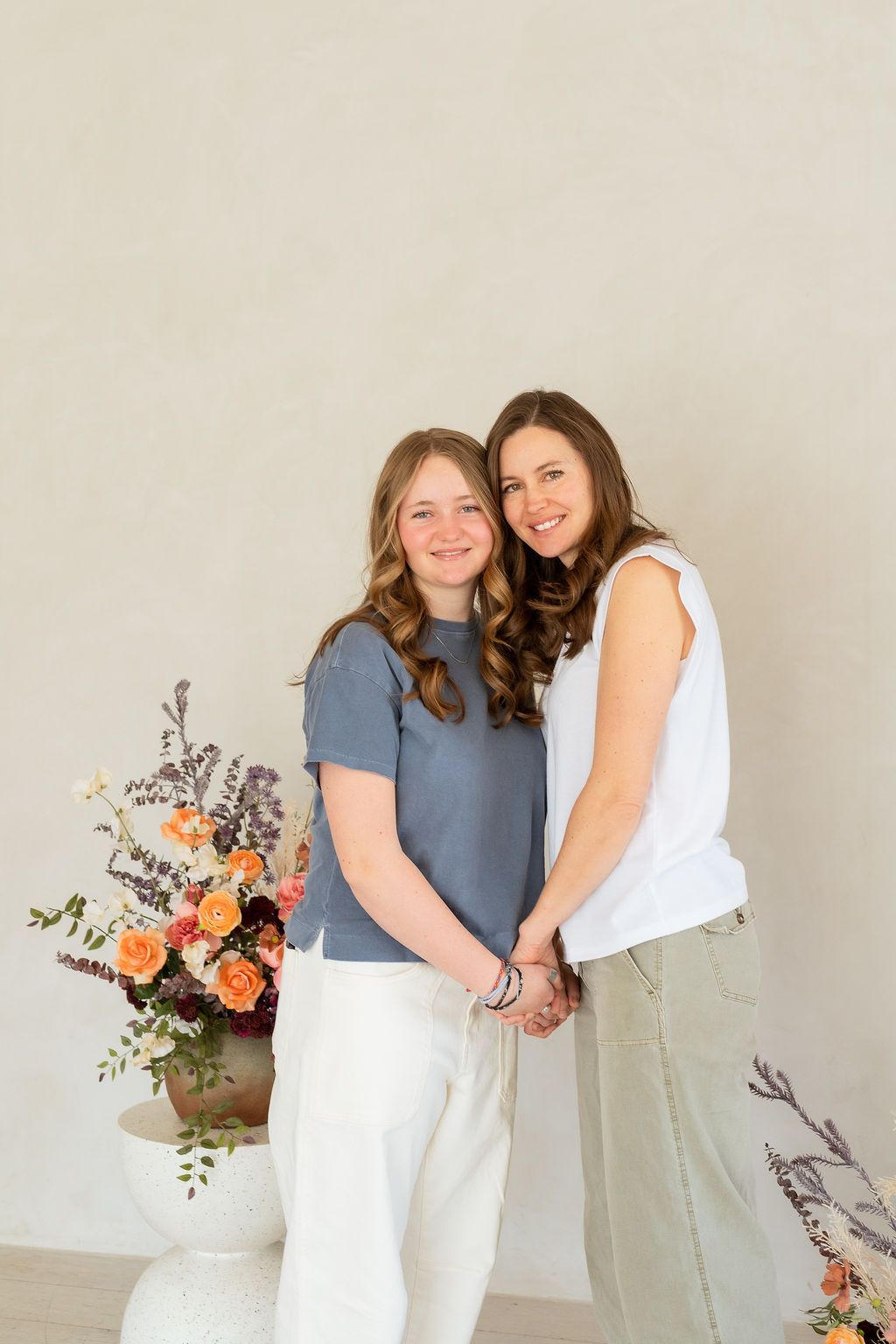 Mother and teenaged daughter embracing next to bouquet of flowers in a white studio during a celebration of motherhood photoshoot
