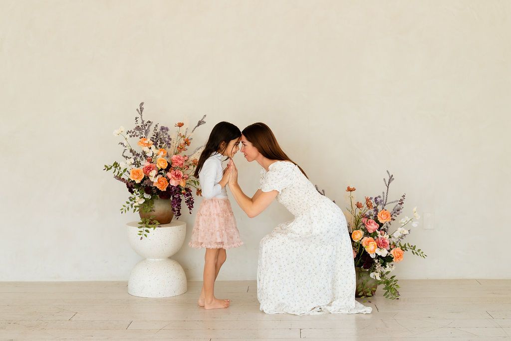 Mom and daughter in white studio with flowers during mother's day minis photoshoot