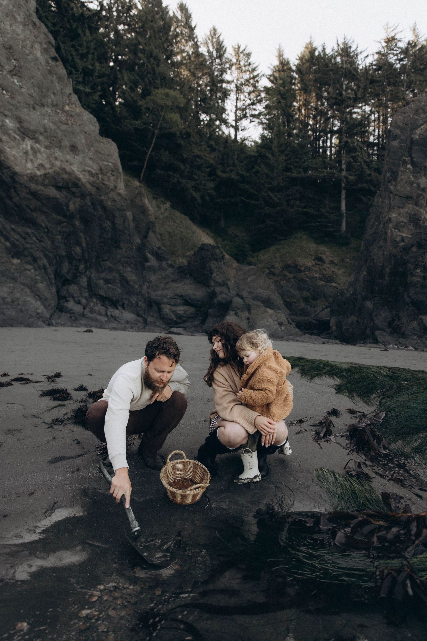 A family of three exploring tide pools on the beach together during an early morning outdoor photoshoot