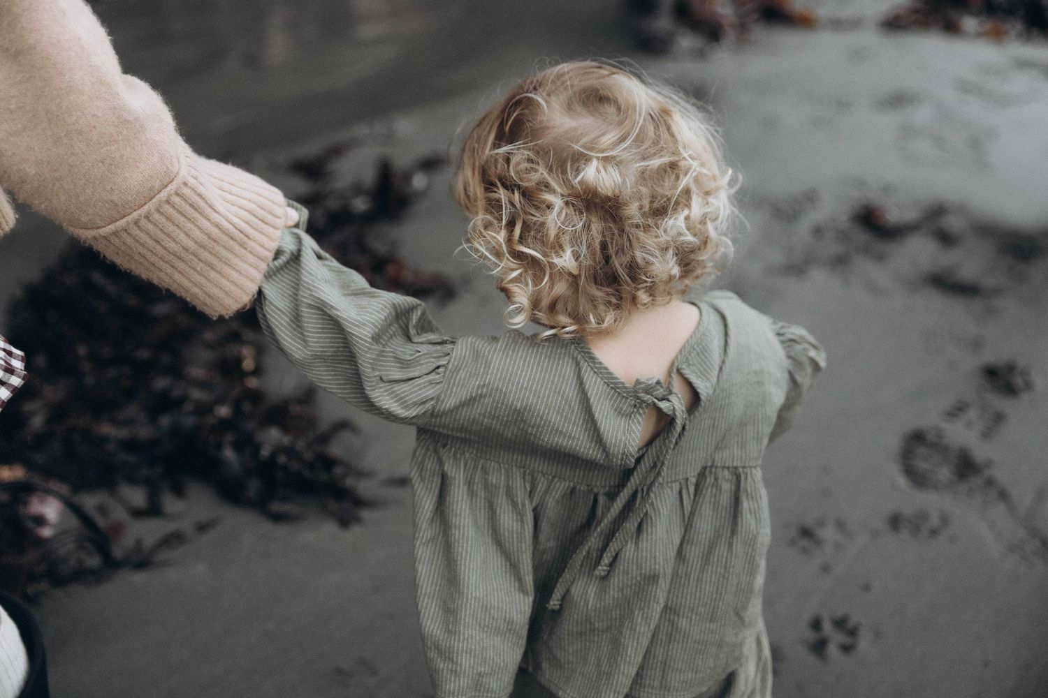 Details of a little girl's blonde curly hair as she explores the beach with her mother during an intimate family photoshoot