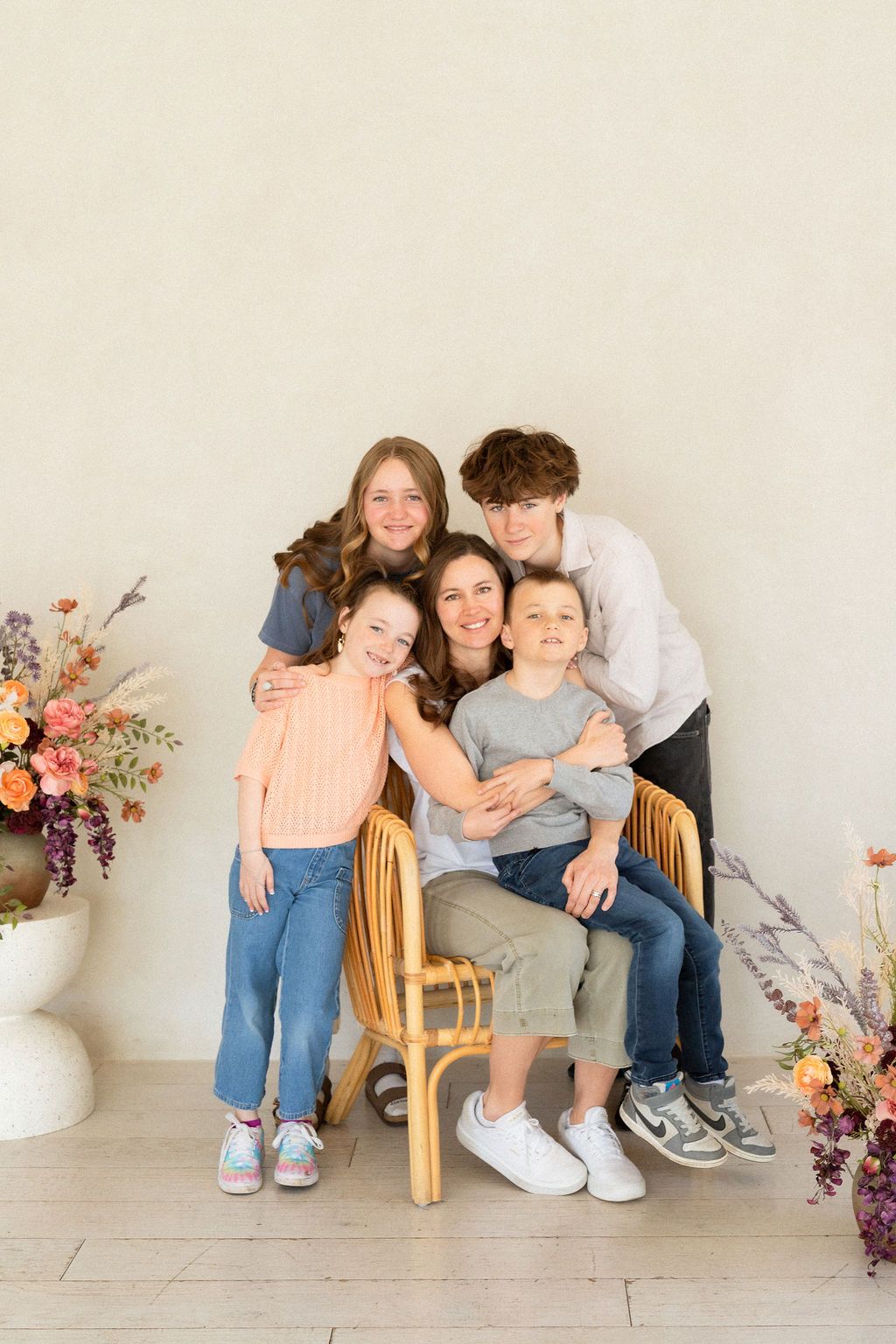 A young mom with her four children from young to teenagers in a white studio with flowers