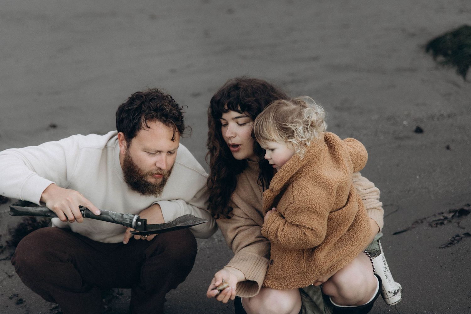 A mom and dad explore the beach at sunrise with their daughter