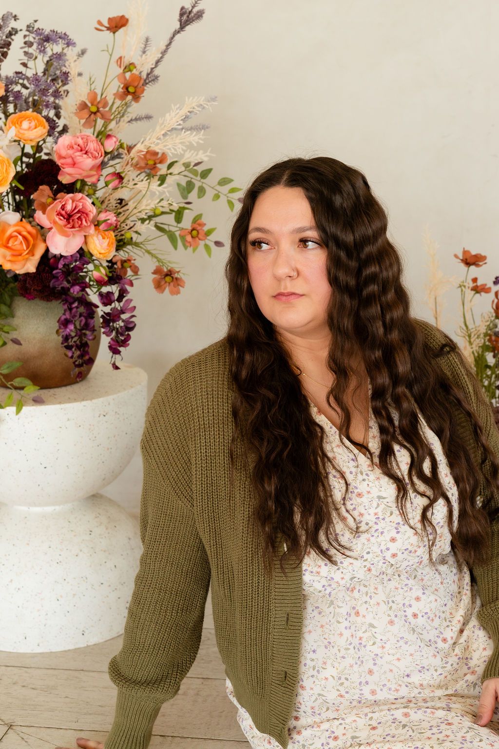 Young woman posing for a mother's day portrait next to colorful flowers in a white studio