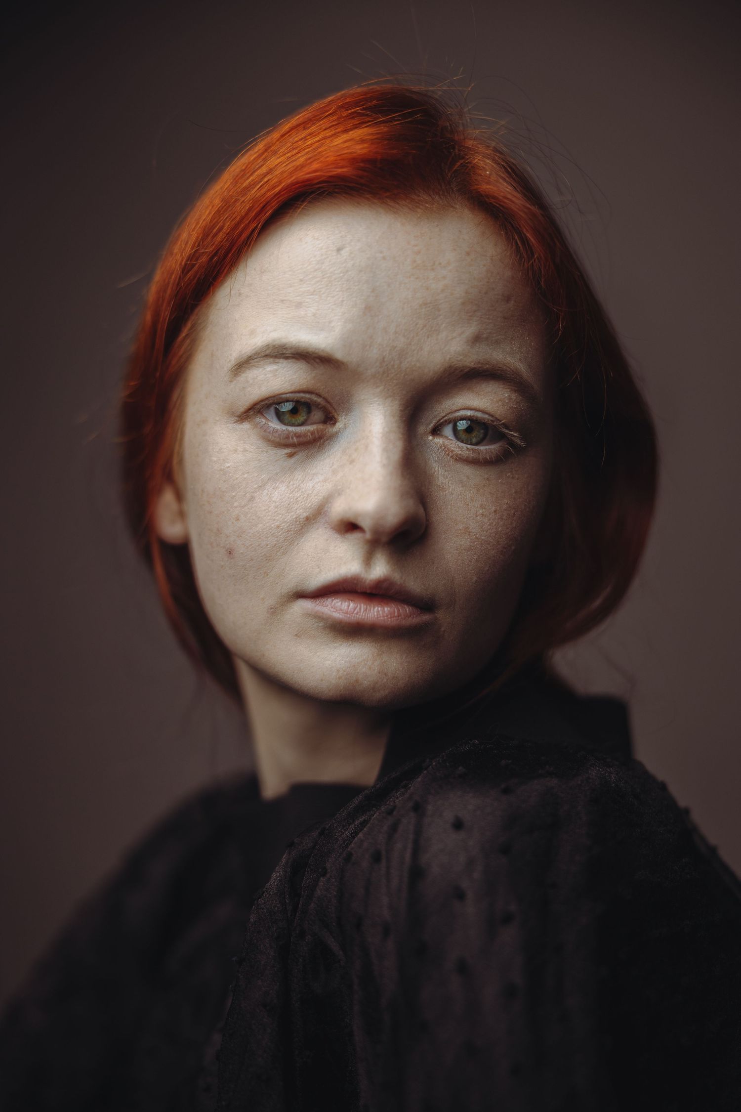 Close-up studio portrait of a freckled redhead woman with a short bob in a black lace blouse.