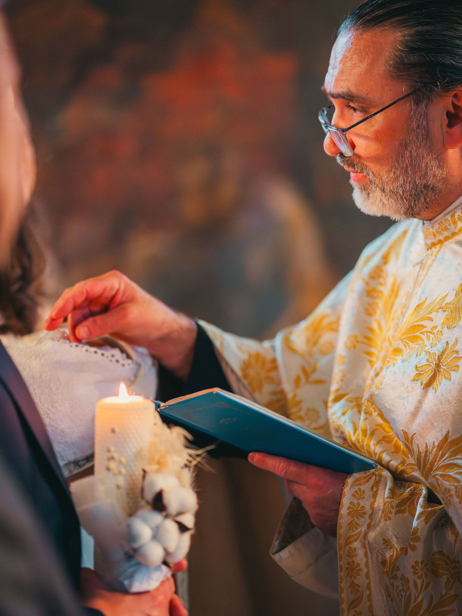 Preot ortodox citind din carte la lumanare in timpul unei ceremonii religioase de botez